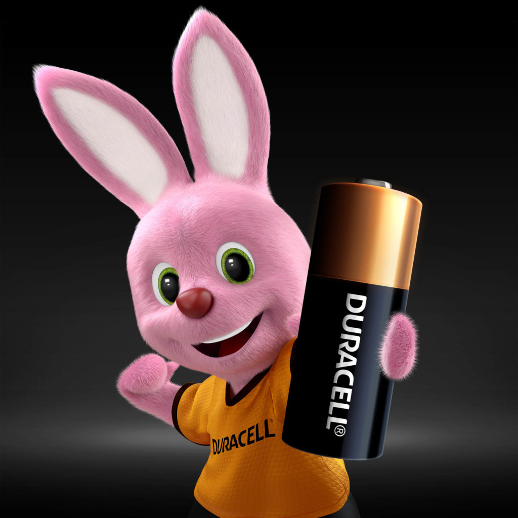 Mascota rosa de Duracell con una pila Duracell. El conejo lleva una camiseta naranja. Fondo oscuro.