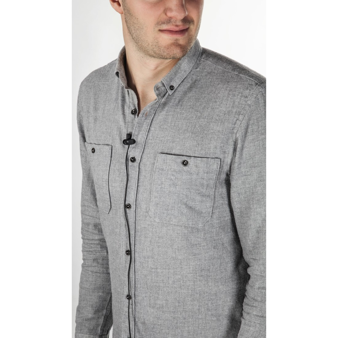 Un uomo indossa una camicia grigia abbottonata. La camicia ha due tasche sul petto. Un microfono nero è attaccato alla camicia.