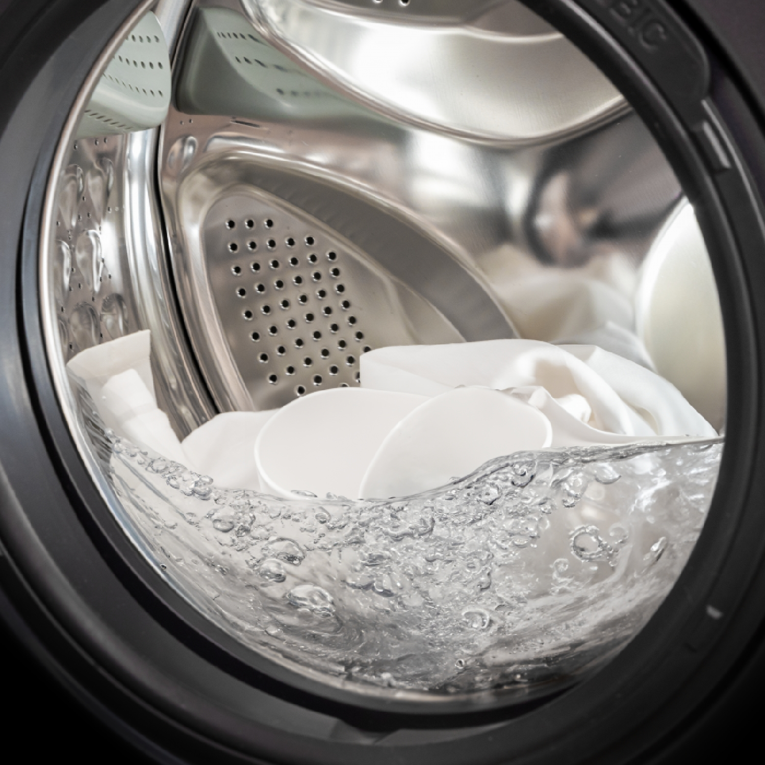 All'interno di una lavatrice. Panni bianchi immersi nell'acqua. Bolle visibili. L'interno della macchina è metallico.
