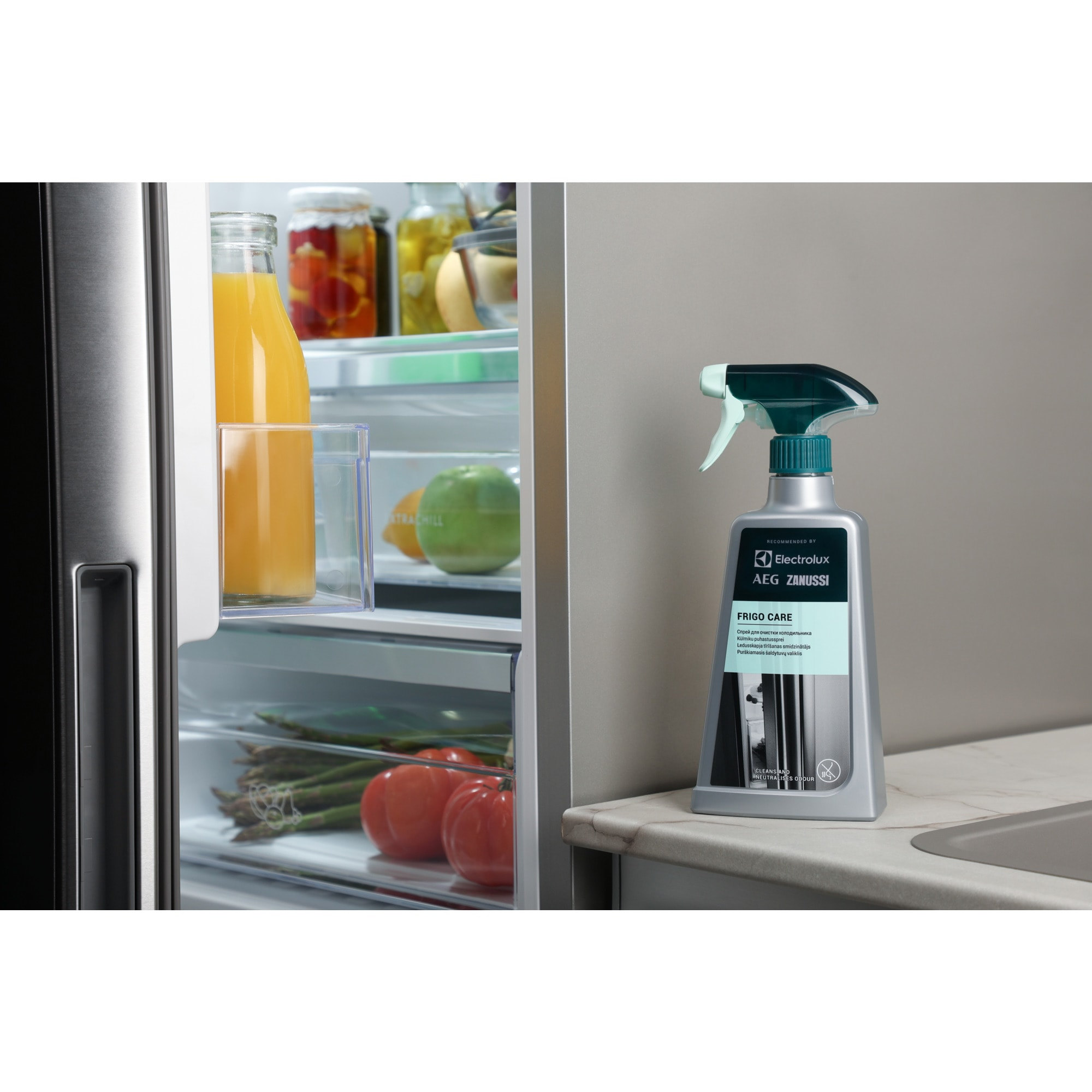 Frigorifero aperto con succo, verdure e barattoli. Accanto, una bottiglia spray per la pulizia.