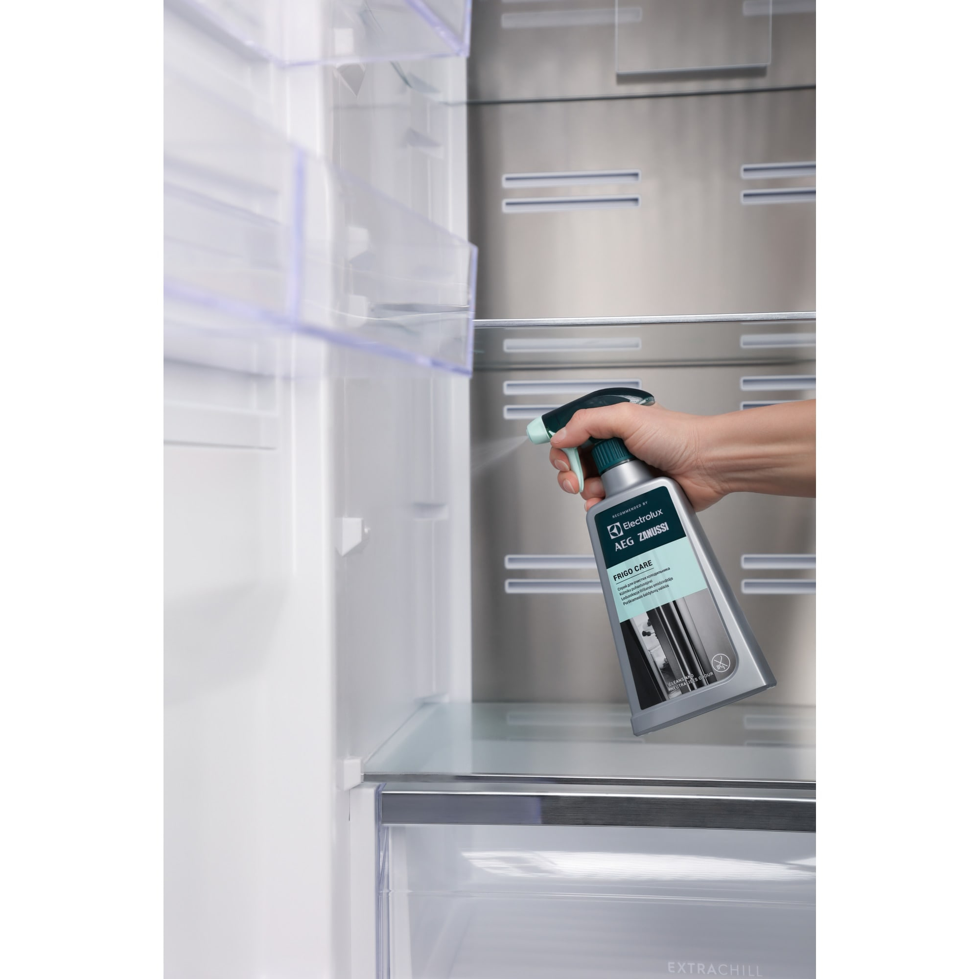 Una mano spruzza all'interno di un frigorifero con un prodotto per la pulizia, Frigo Care, di Electrolux AEG Zanussi.