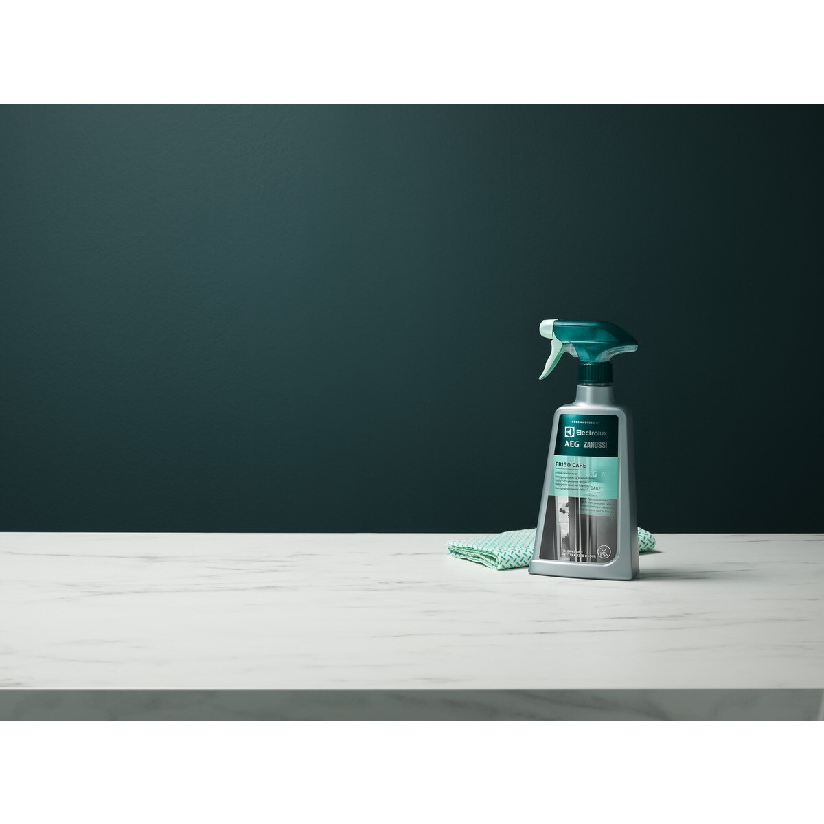 Una bottiglia di Electrolux AEG Zanussi Frigo Care su una superficie bianca con un panno verde, su sfondo verde scuro.