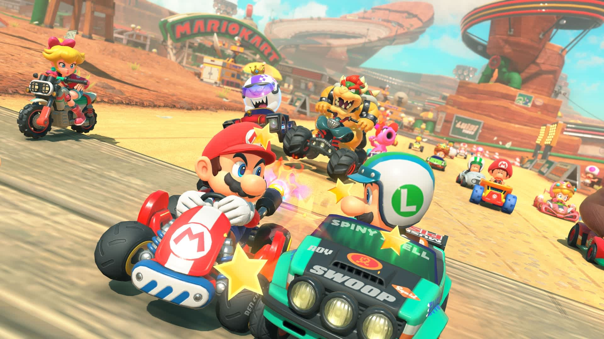 Scena z Mario Kart. Mario i Luigi ścigają się w gokartach. Peach na motocyklu. Bowser i inne postacie ścigają się w tle.