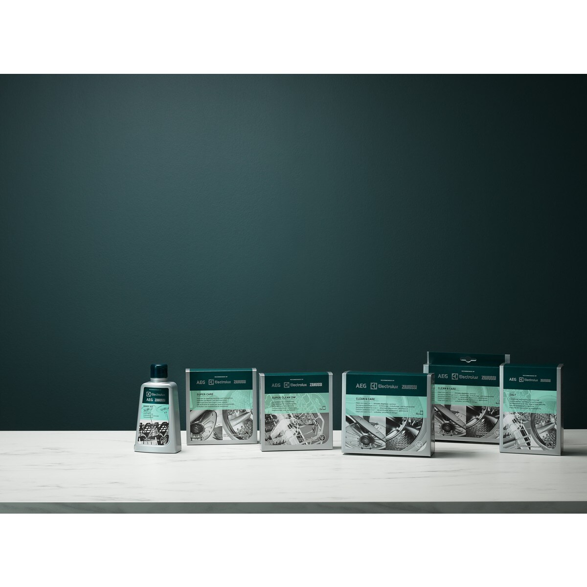 Produkty na białej powierzchni na tle turkusowego tła. Obecnych jest kilka pudełek i butelka, z widocznymi nazwami produktów.