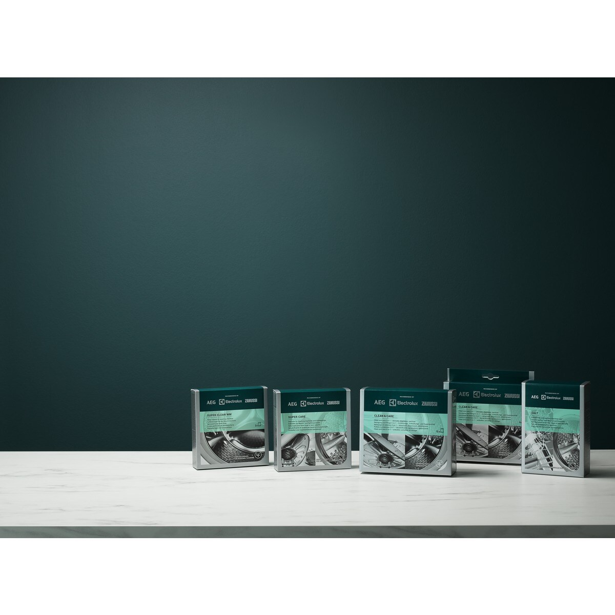 Kilka pudełek produktów AEG Electrolux na białej powierzchni. Tło to ciemnozielona ściana.