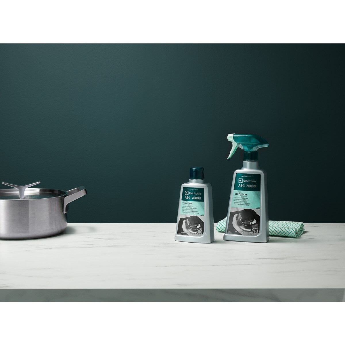 Garnek, spray czyszczący i butelka na białej powierzchni z ciemnozielonym tłem.