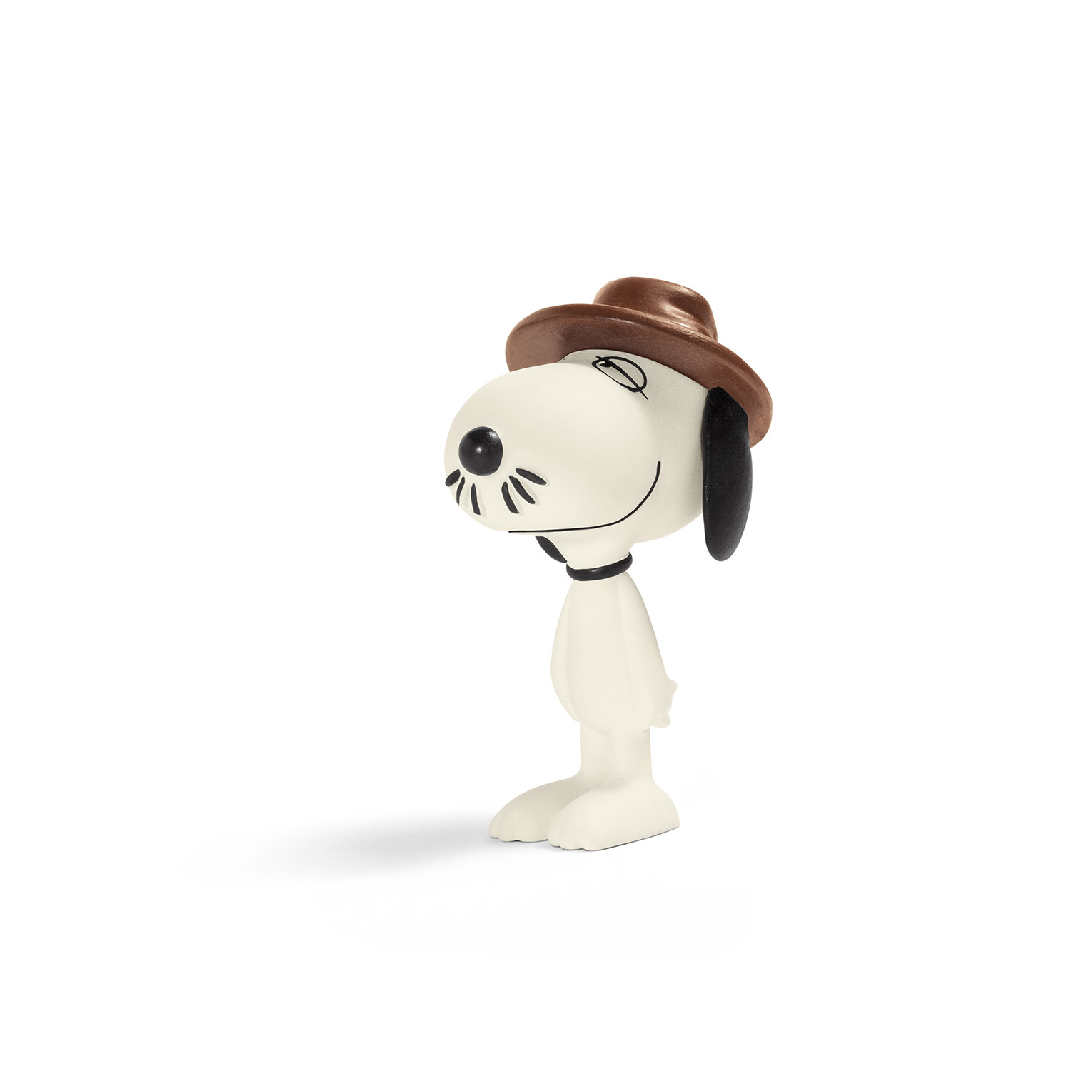 Statuetta di Snoopy con cappello marrone, sorridente. Orecchie e naso neri. Corpo bianco, su superficie bianca, sfondo bianco.