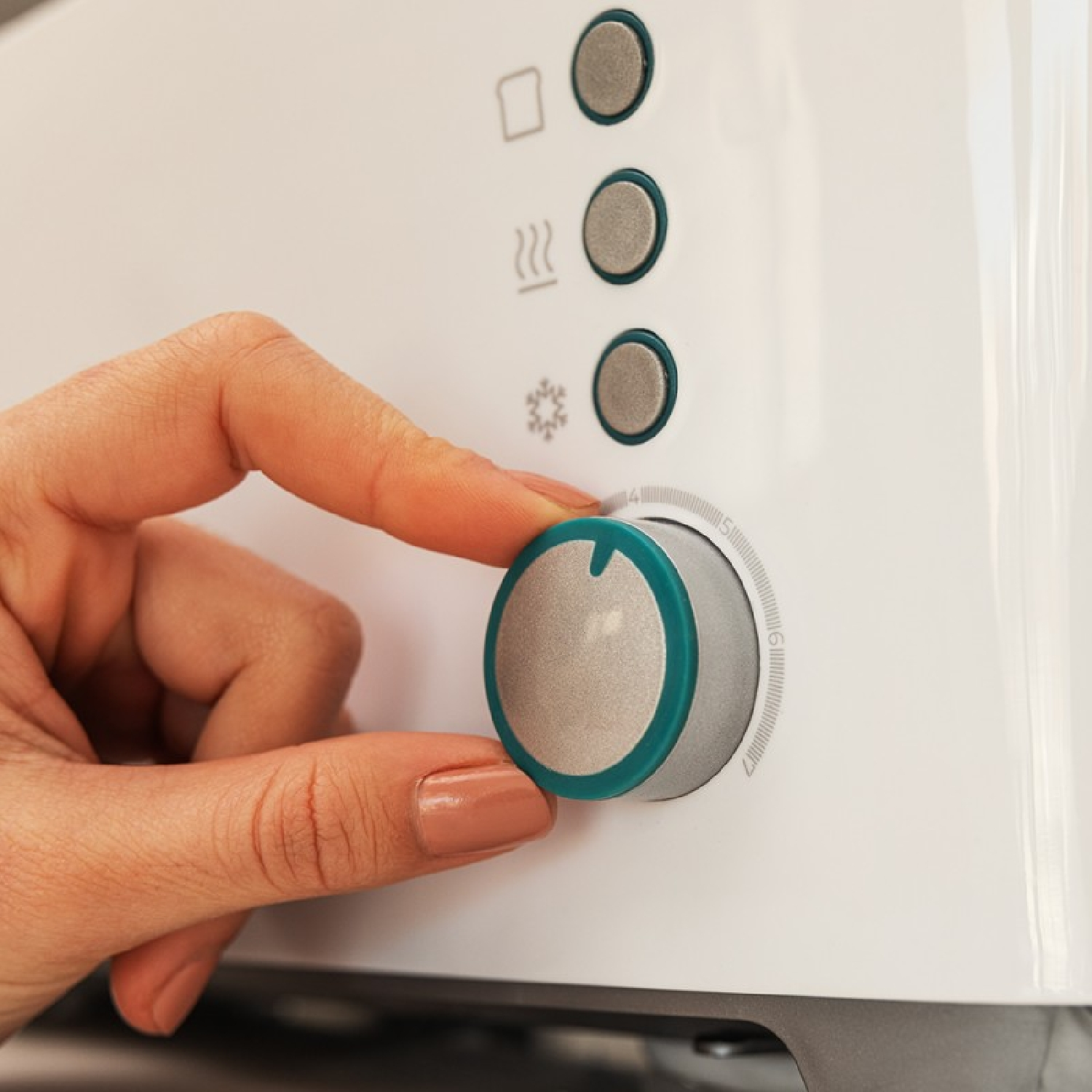 Ręka obraca pokrętło na białym urządzeniu. Pokrętło ma zielony pierścień. Nad nim znajdują się trzy srebrne przyciski.