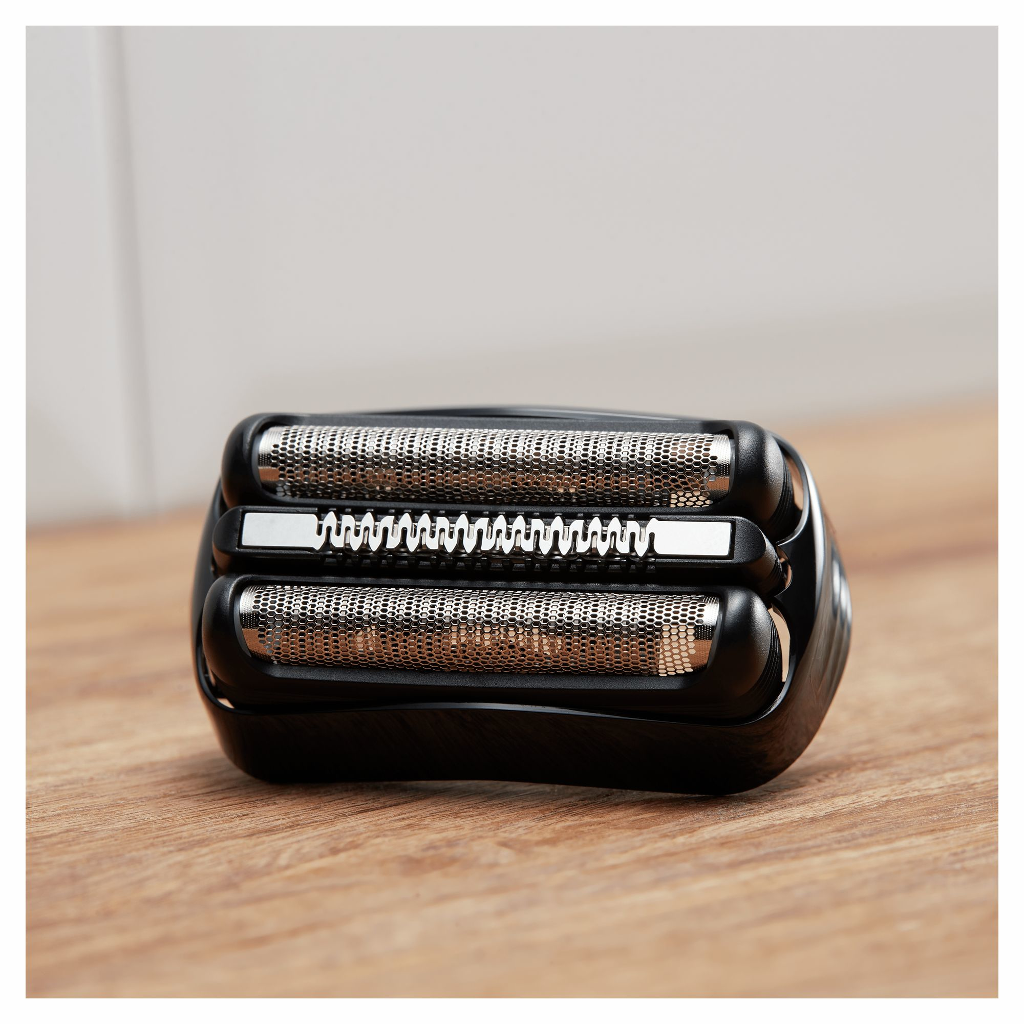 Zbliżenie czarnej głowicy golarki elektrycznej ze srebrną siatką i ostrzami na drewnianej powierzchni.