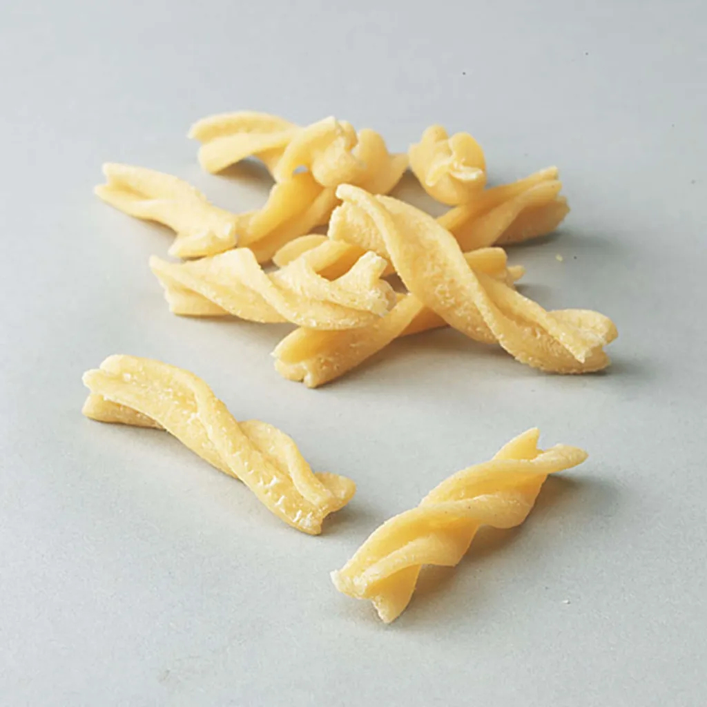 Nahaufnahme von ungekochter Pasta. Mehrere gelbe Fusilli-Nudeln liegen auf einer hellgrauen Oberfläche.