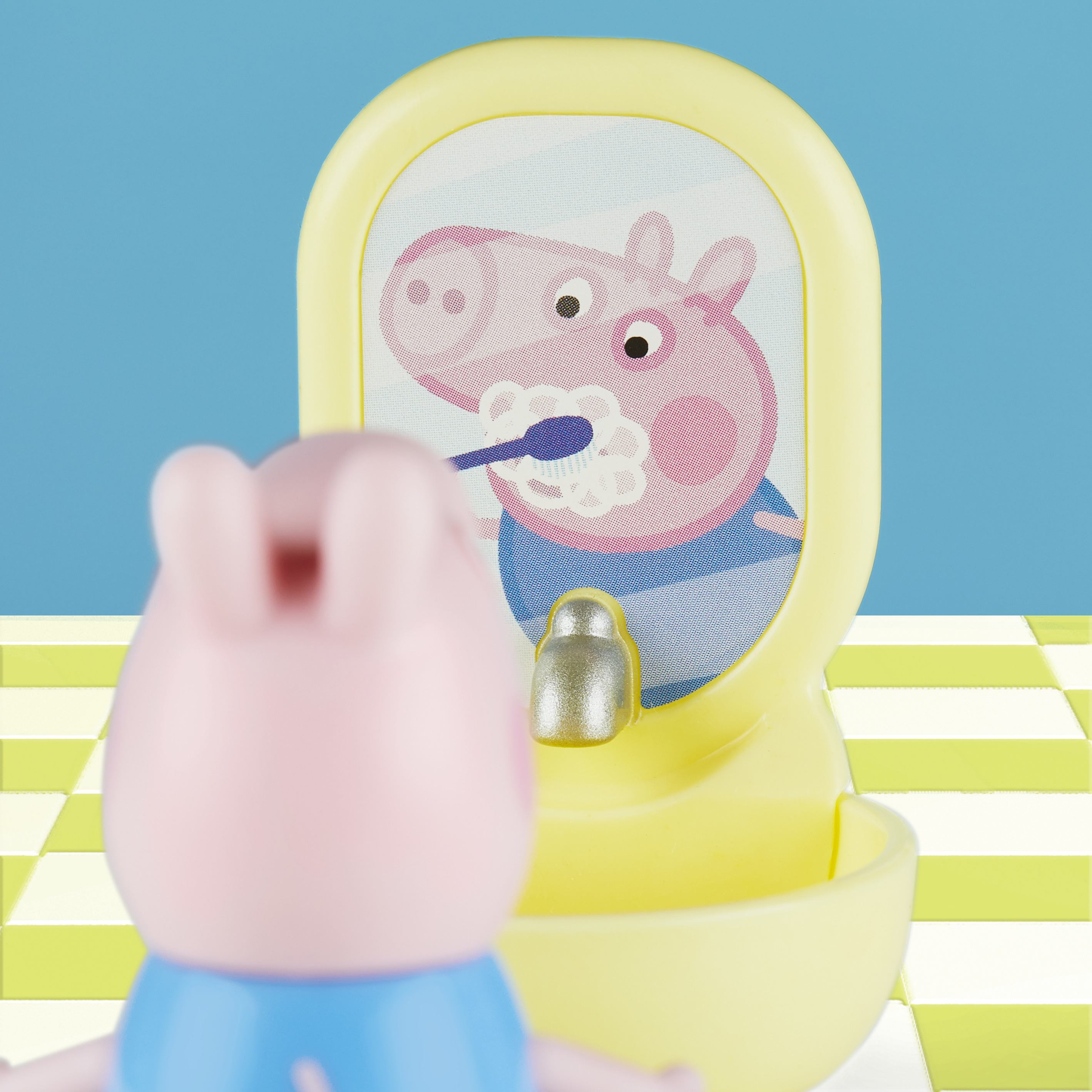 Un giocattolo di Peppa Pig si guarda allo specchio mentre Peppa Pig si lava i denti. Un lavandino giallo davanti a uno sfondo blu.