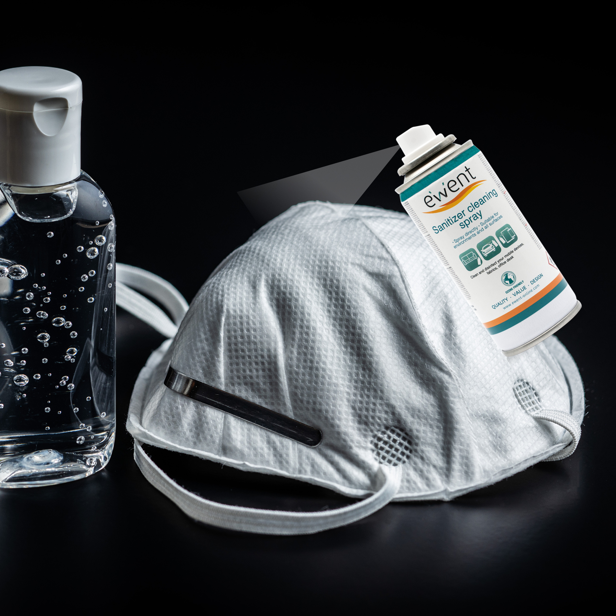 Maska, spray do dezynfekcji i płyn do dezynfekcji rąk na czarnej powierzchni. Spray rozpyla się na masce.