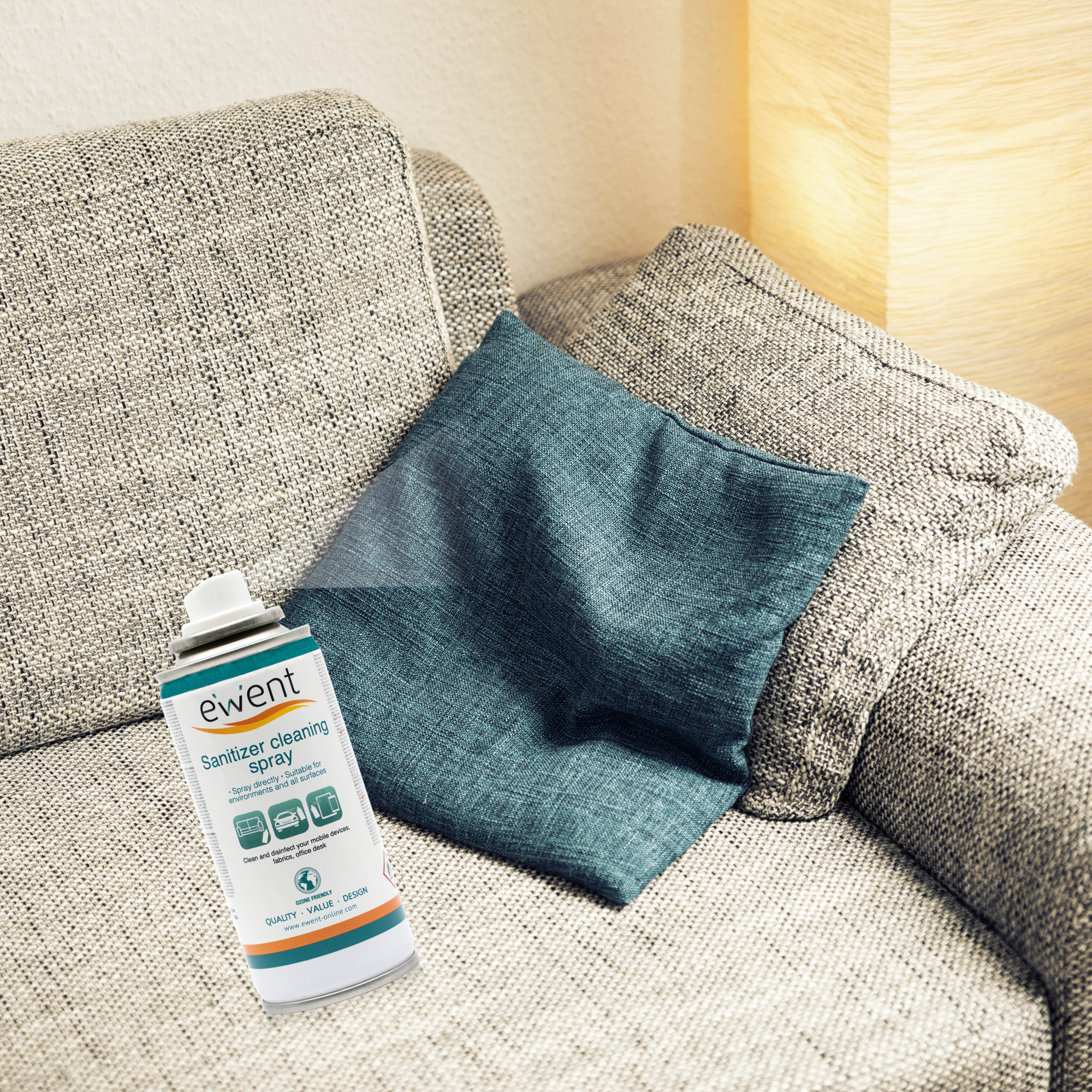 Puszka sprayu do dezynfekcji na kanapie z poduszkami. Kanapa i poduszki są szare i niebiesko-zielone.