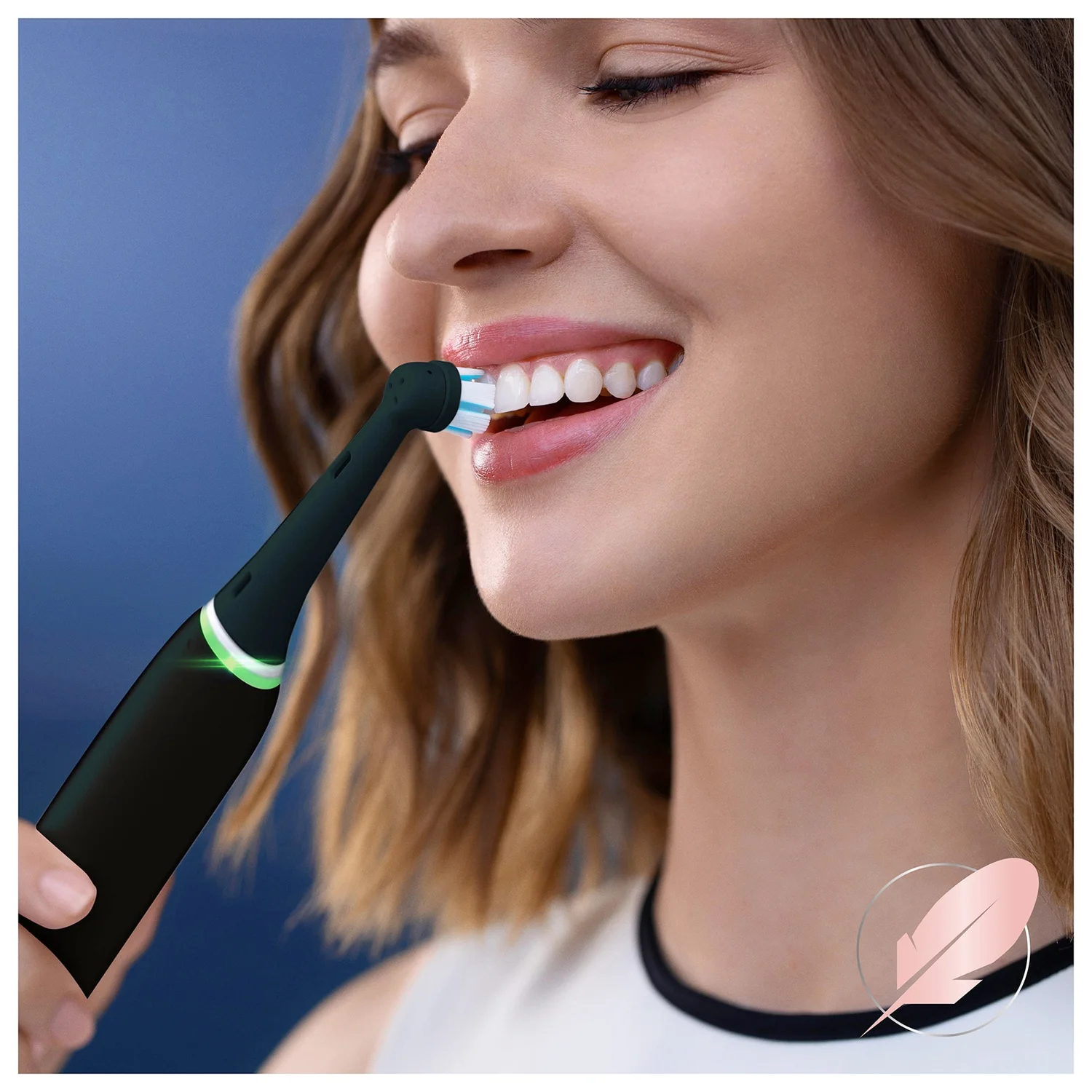 Kobieta uśmiecha się, szczotkując zęby czarną elektryczną szczoteczką. Tło to gradient niebieskiego.