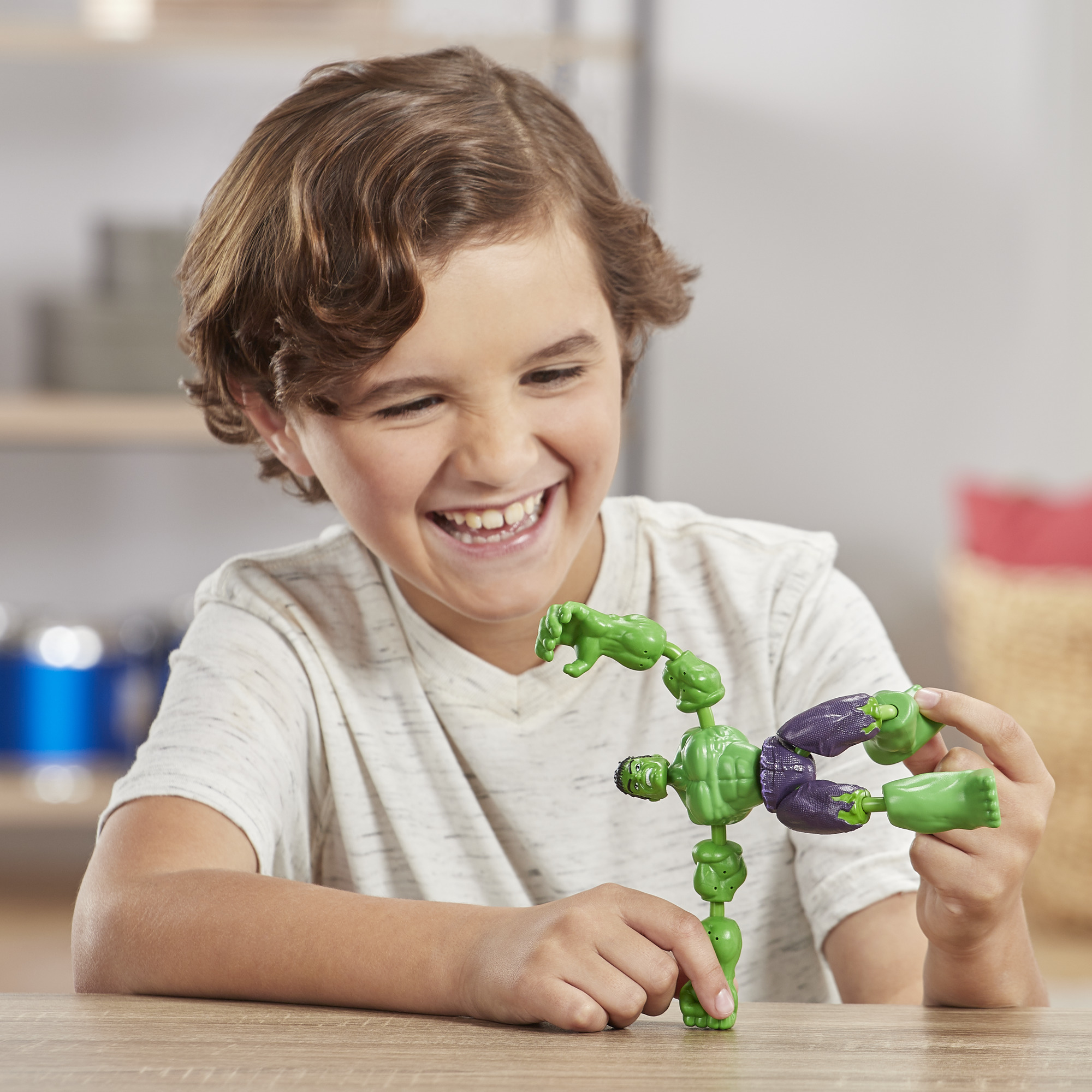 Un ragazzo sorride, gioca con un pupazzo di Hulk. La figura è verde con pantaloni viola. Il ragazzo è seduto a un tavolo.