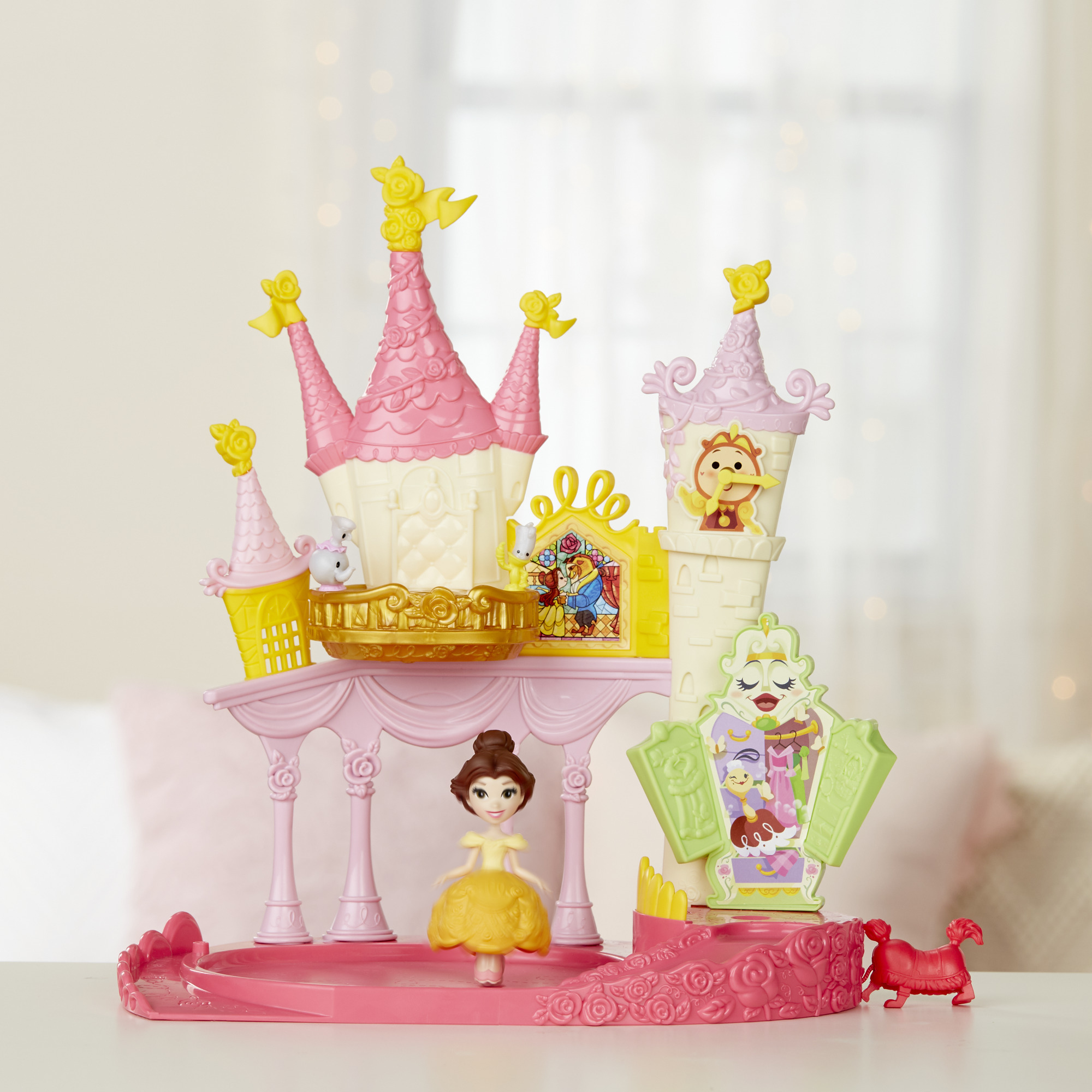 Castello giocattolo con bambola Belle, cane rosso e personaggi dei cartoni animati. I colori rosa e giallo dominano, con sfondo bianco.