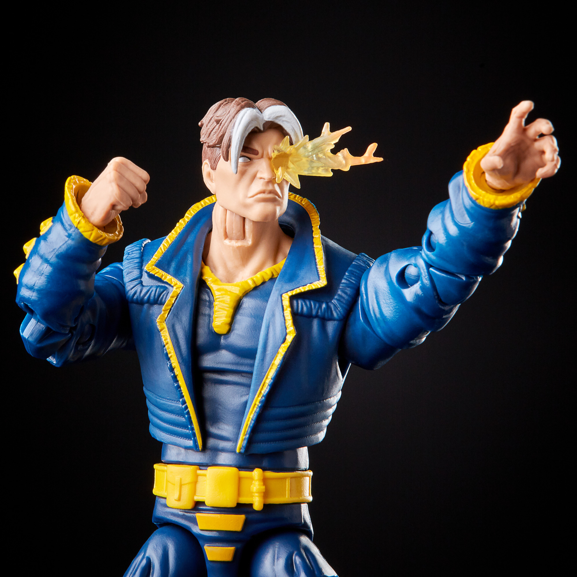 Action figure di un uomo in abito blu e giallo, occhio con esplosione di energia gialla, pugno chiuso, braccio teso, sfondo nero.