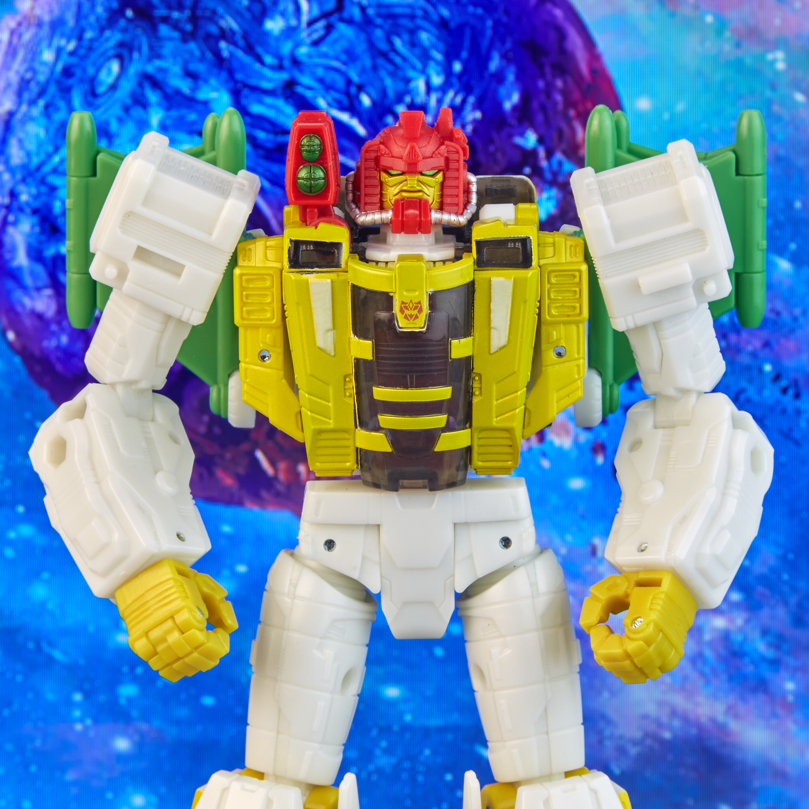 Un giocattolo robot giallo, bianco e rosso si erge su uno sfondo blu. Ha una testa rossa e elementi verdi simili ad ali.