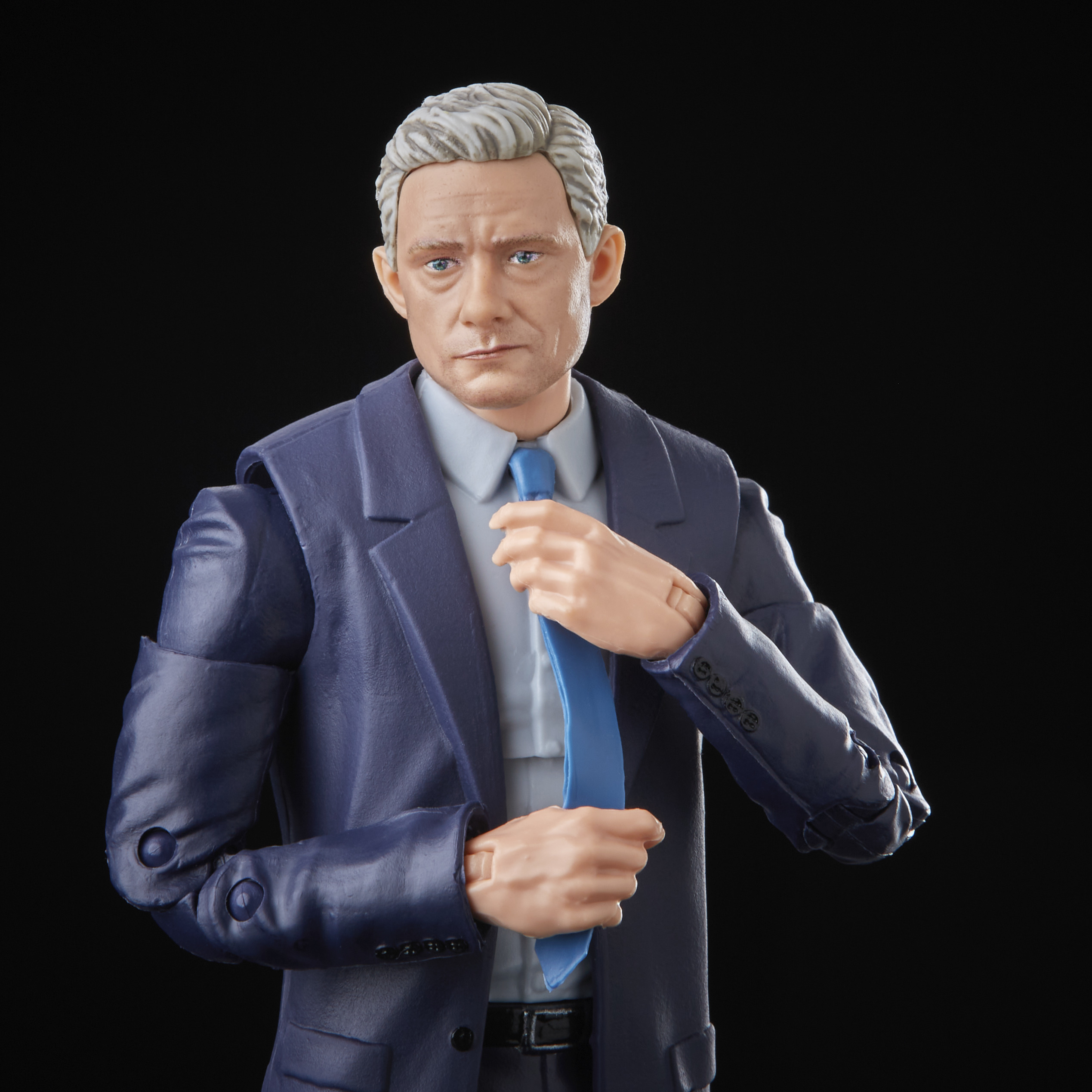 Una statuina di un uomo in abito blu che si sistema la cravatta blu, su sfondo nero.
