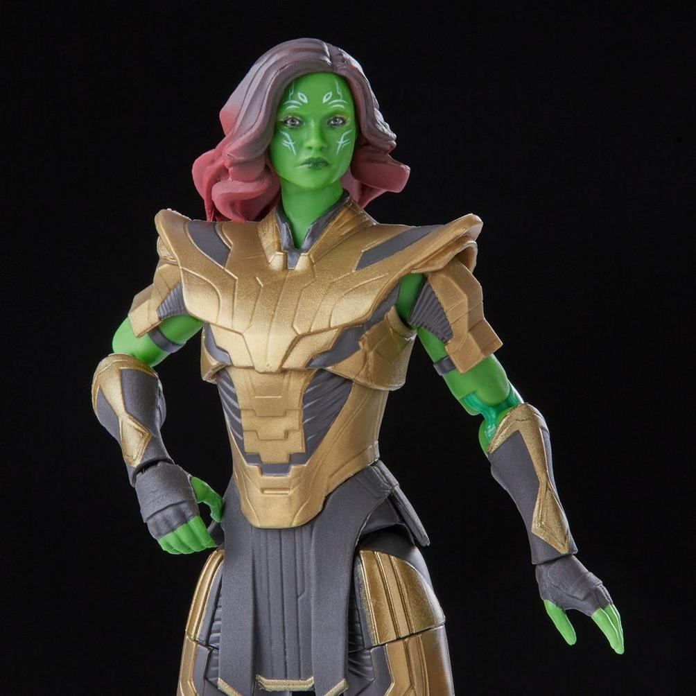 Una figura de acción de Gamora con piel verde, cabello rojo-púrpura y armadura dorada se alza sobre un fondo negro.