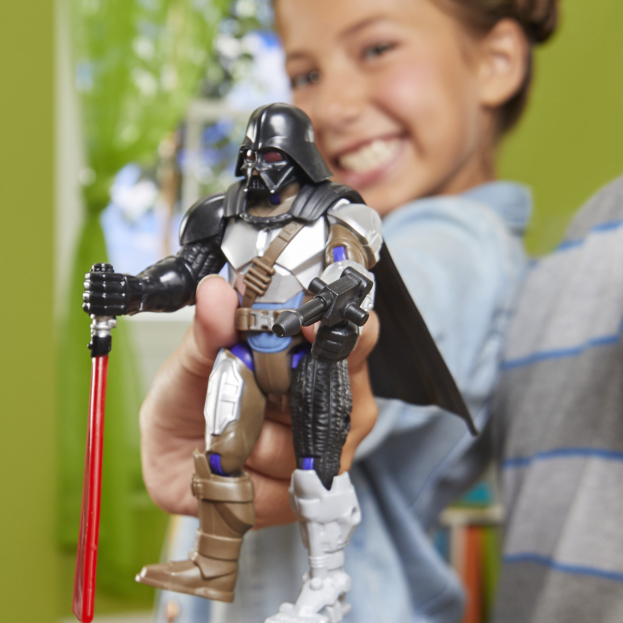 Un niño sostiene una figura de acción de Darth Vader. La figura tiene un sable de luz rojo y un bláster. El niño sonríe.