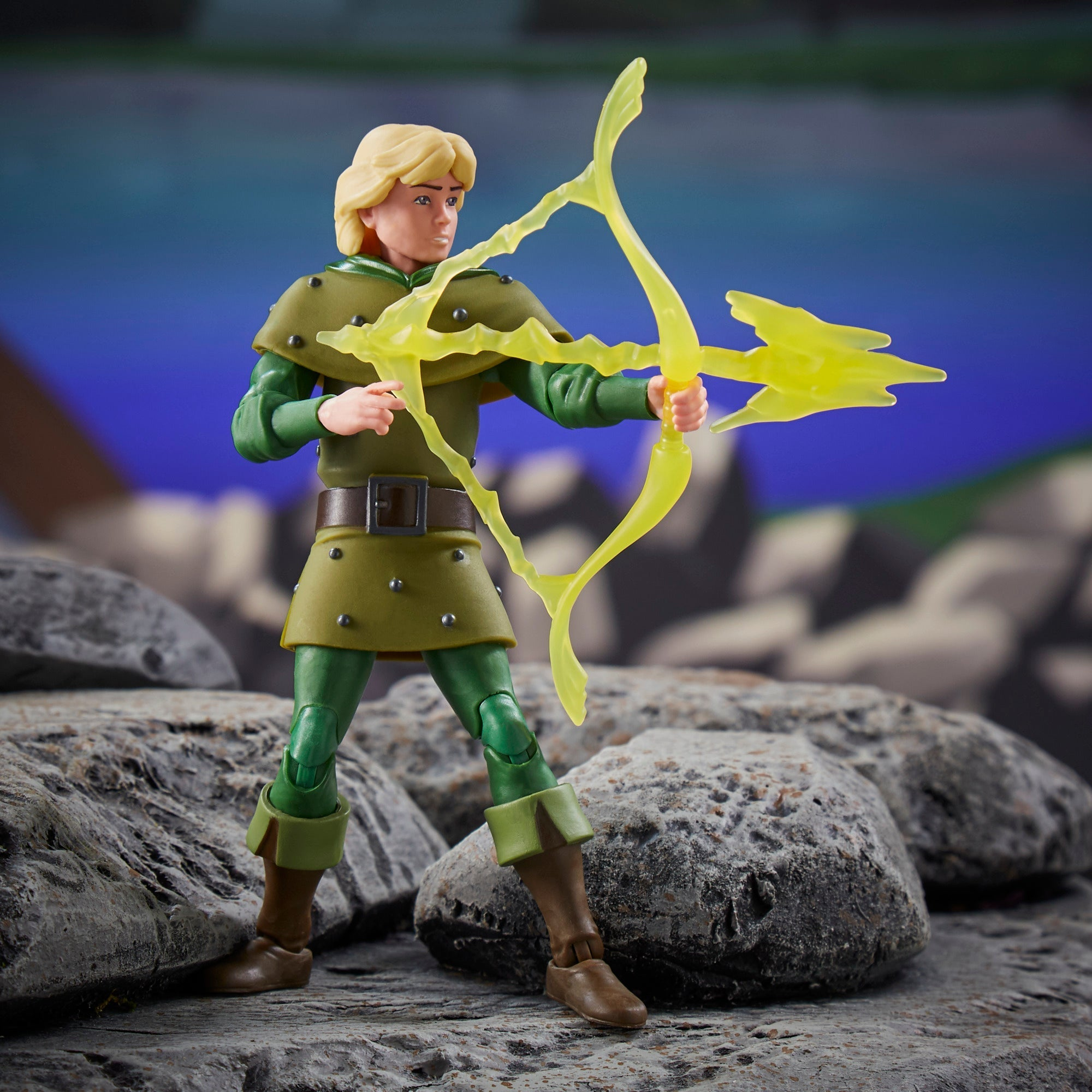 Una figura di un uomo in armatura verde che punta un arco giallo brillante. È in piedi su rocce grigie, con uno sfondo sfocato.