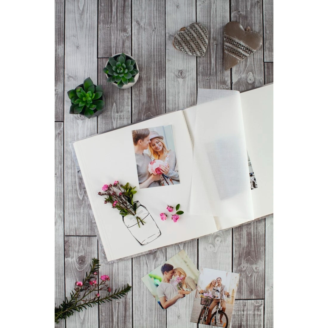 Ein offenes Fotoalbum mit Bildern eines Paares, Blumen und dekorativen Herzen auf einem Holzgrund.