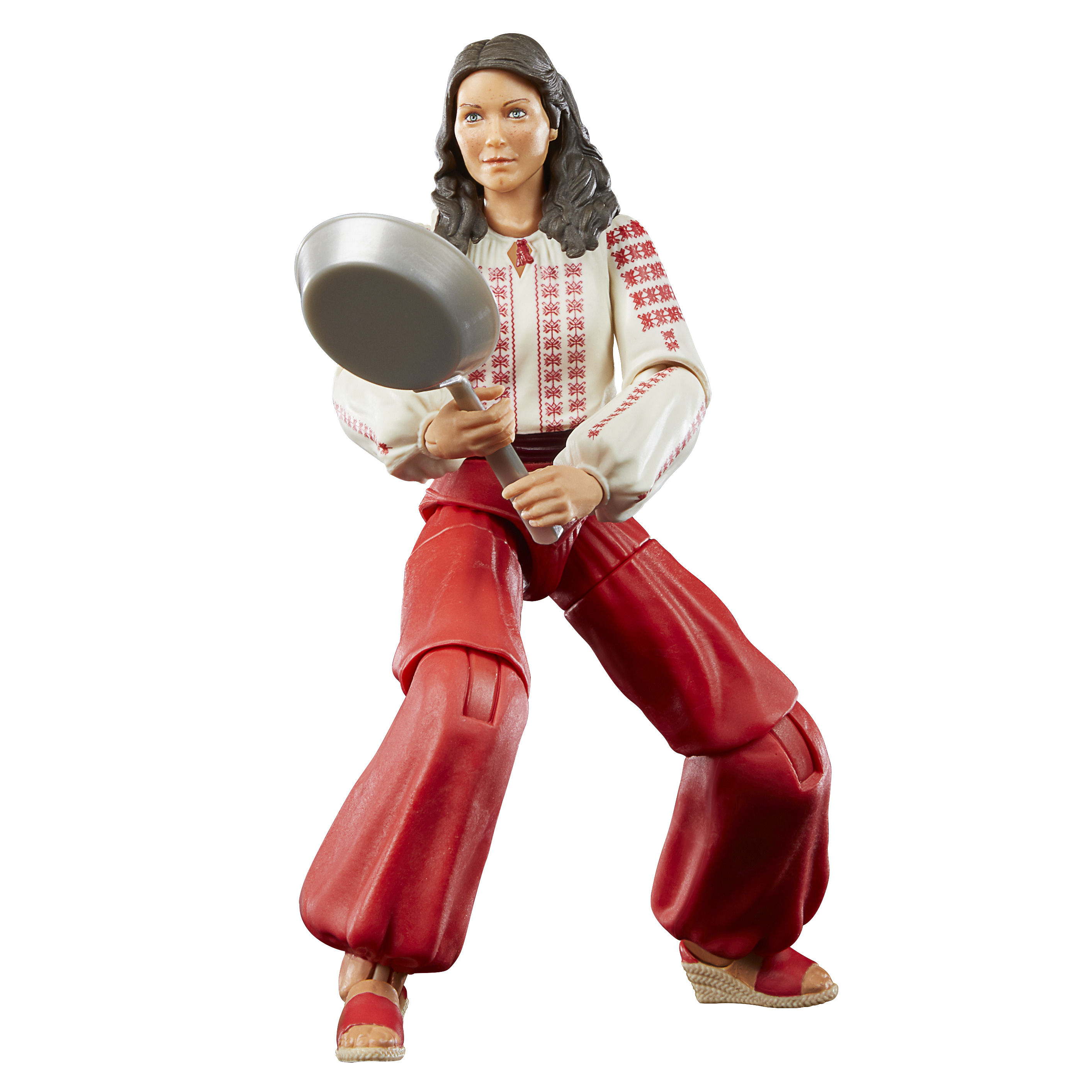 Una statuina di una donna in abiti tradizionali, che tiene in mano una padella. Il suo abito è bianco con ricami rossi e pantaloni rossi.