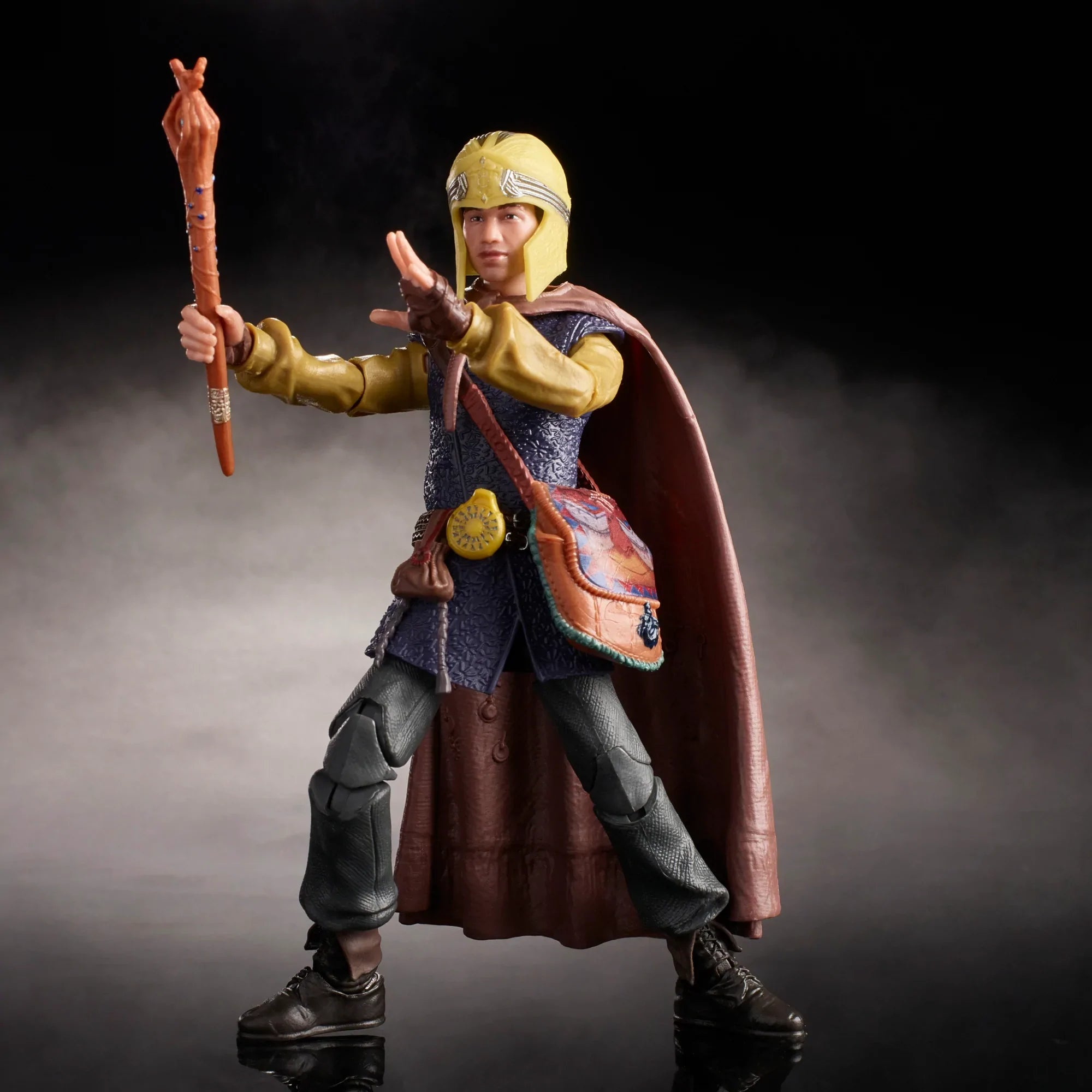Una figura in abito medievale, con un bastone. Indossa elmo, mantello e una borsa. Sfondo scuro.