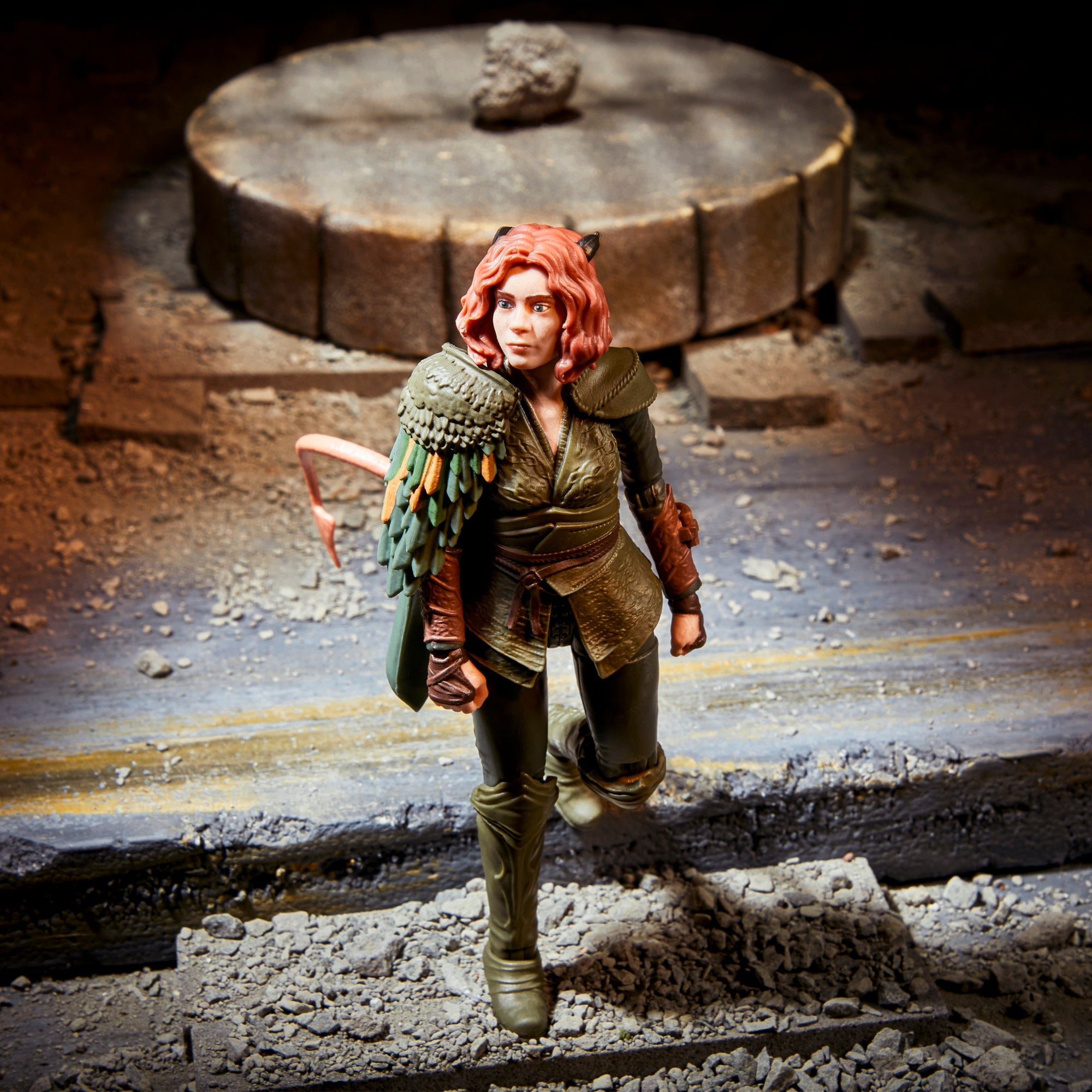 Eine weibliche Actionfigur, rotes Haar, Katzenohren, grünes Outfit, steht auf felsigem Untergrund, mit Stein Hintergrund.