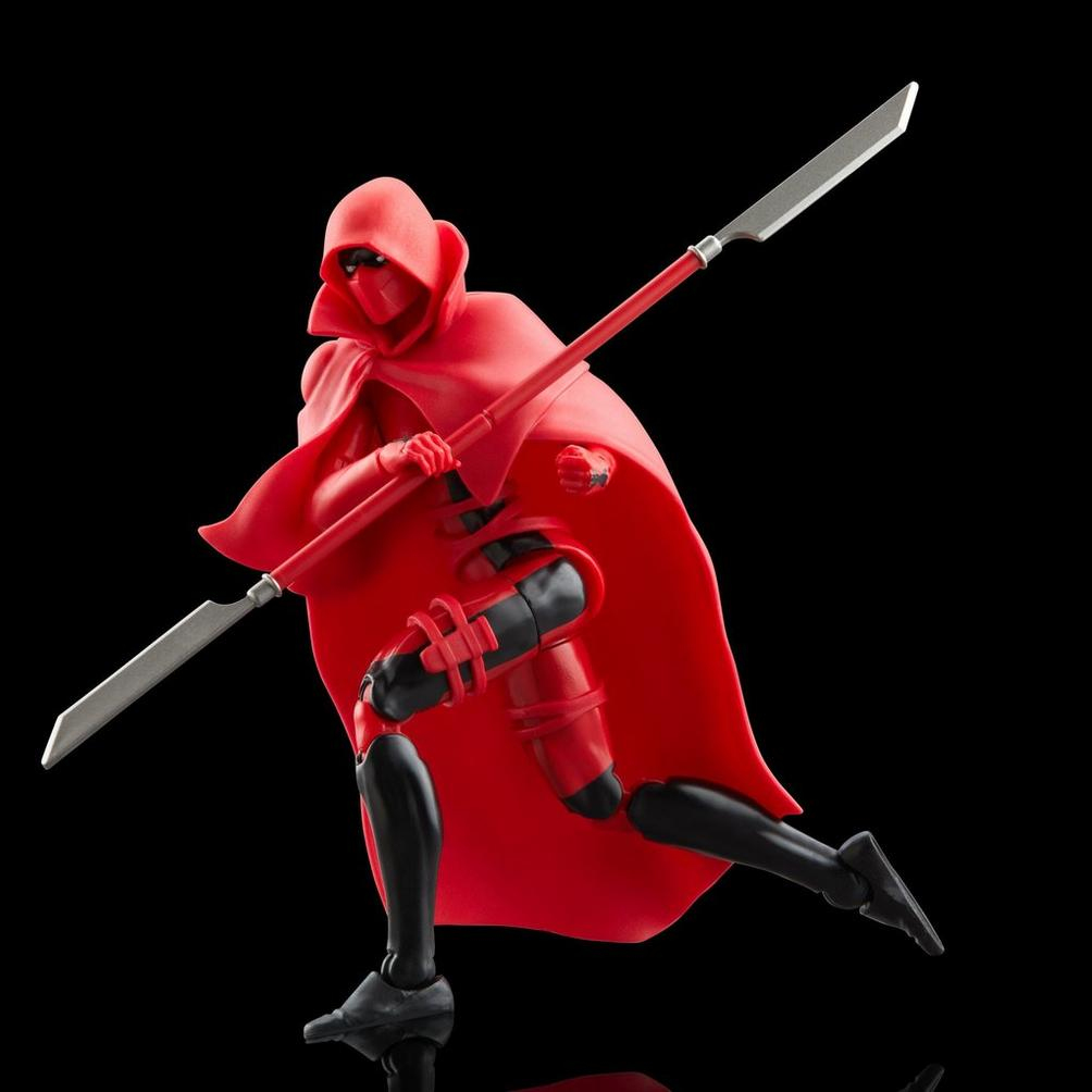 Una figura rossa con mantello con cappuccio tiene una lancia. La figura è in posa dinamica su sfondo nero. La lancia ha una lama d'argento.