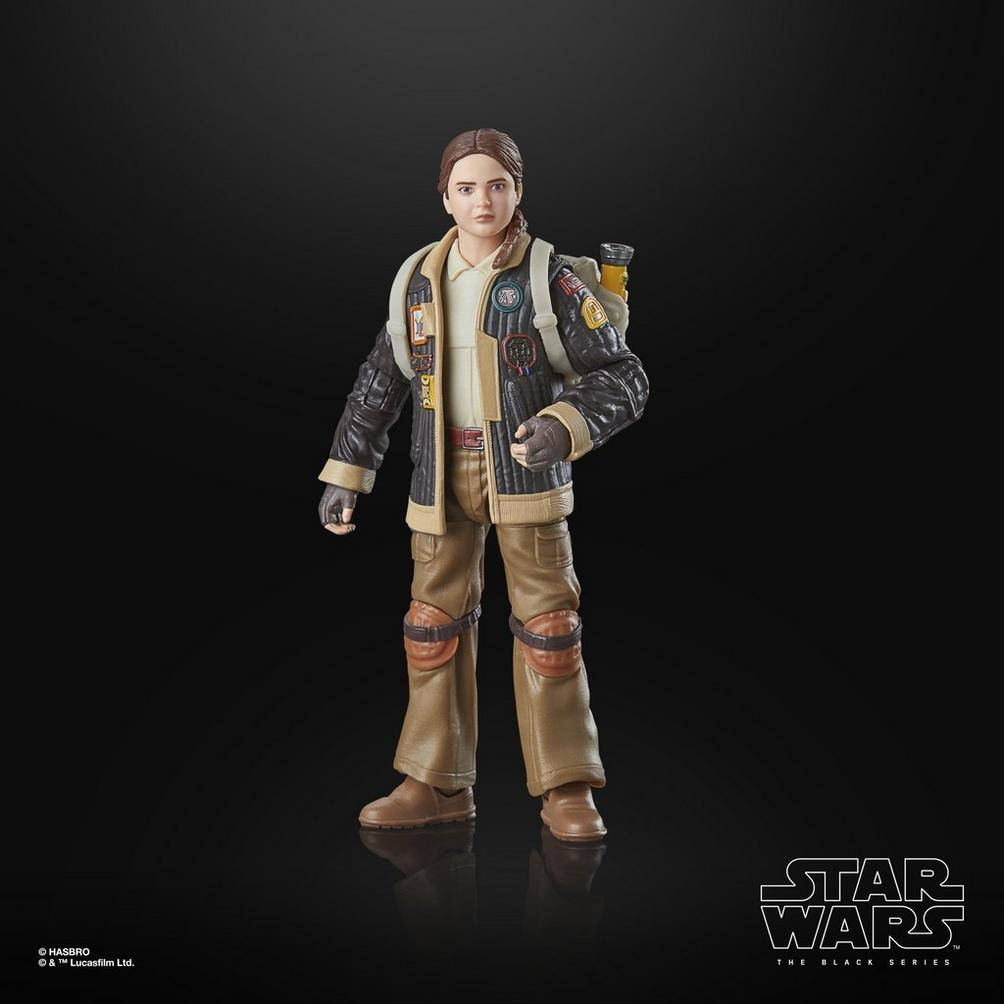 Ceket ve pantolon giymiş, sırt çantası olan bir Star Wars aksiyon figürü. Figür siyah bir yüzeyde duruyor.