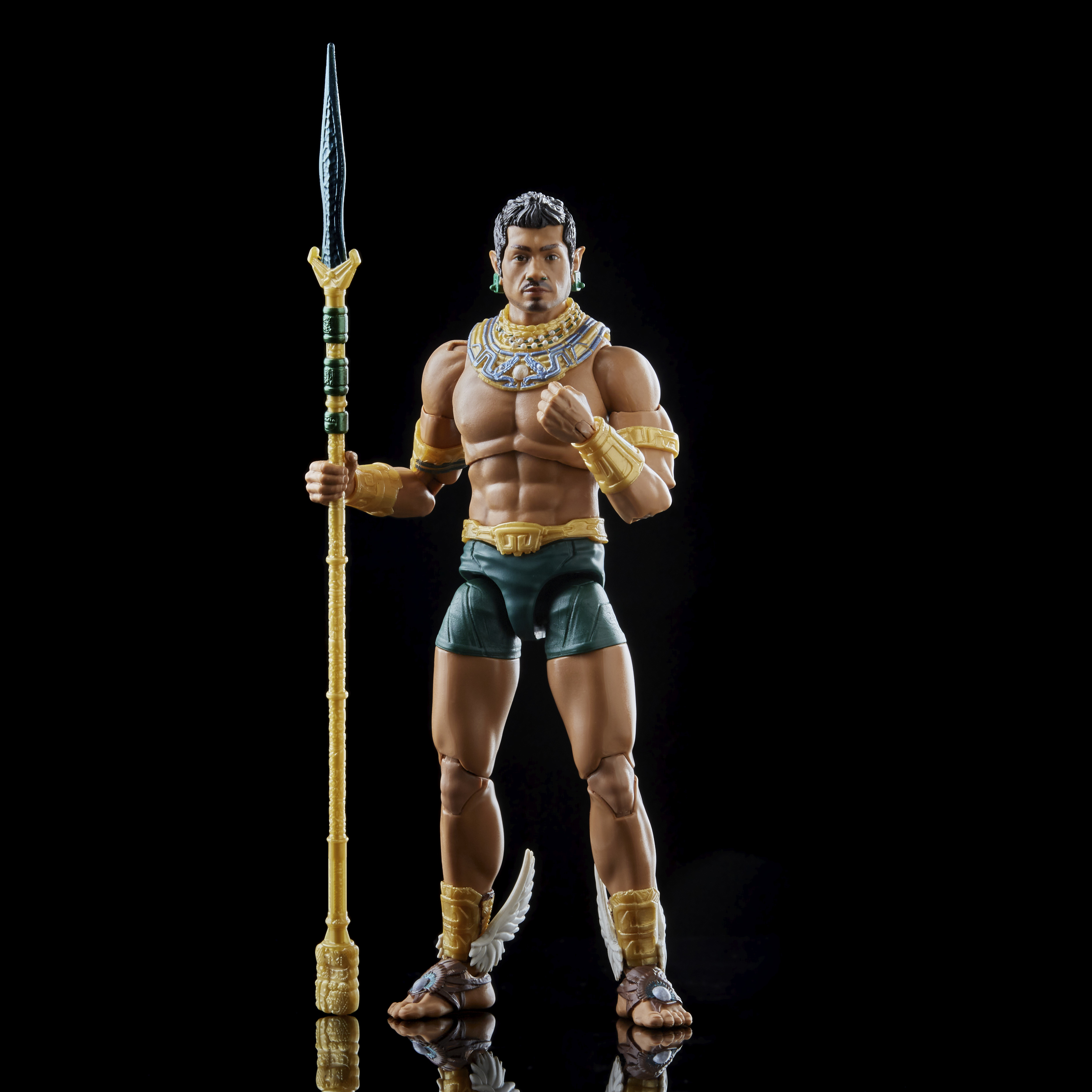 Action figure di un uomo con una lancia. Indossa gioielli oro e blu e pantaloncini verdi, su sfondo nero.
