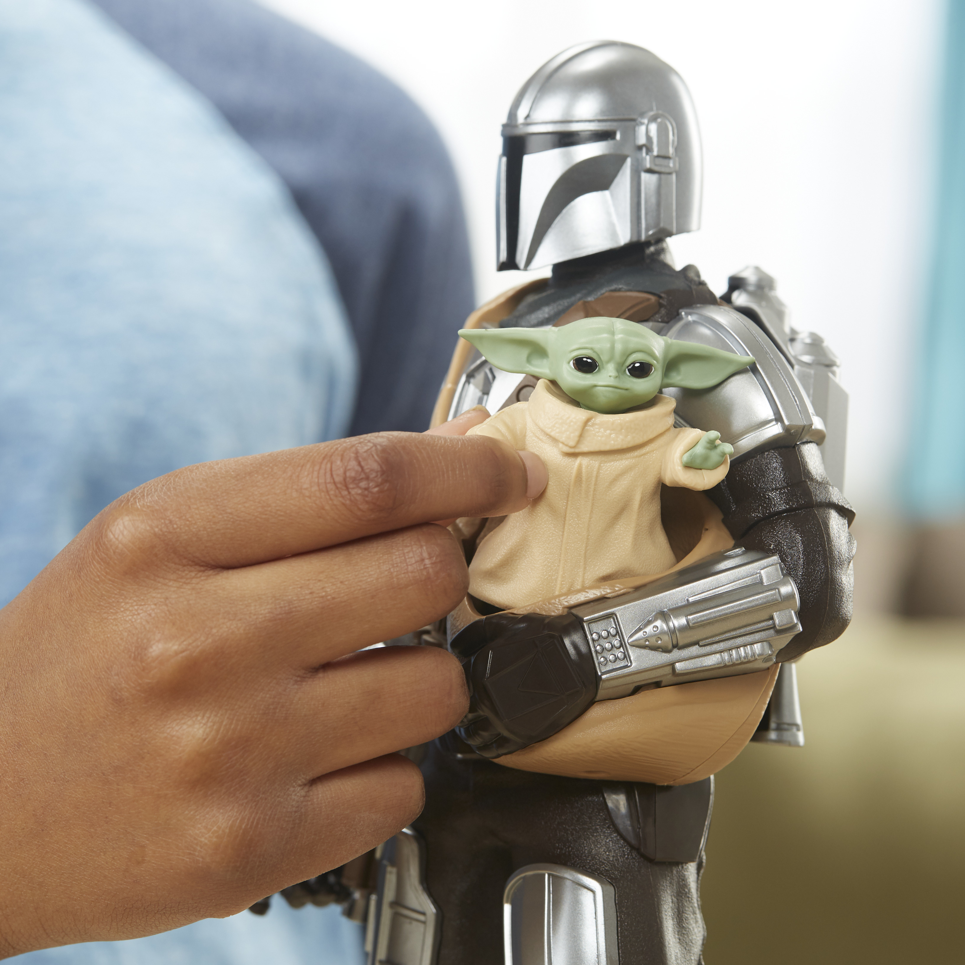 Una persona tiene in mano un personaggio giocattolo Mandaloriano con un personaggio di Baby Yoda tra le braccia. I personaggi sono dettagliati.