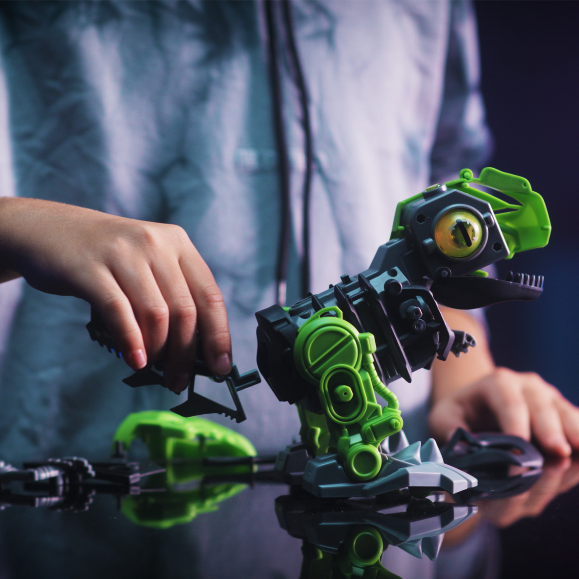 Un bambino sta assemblando un giocattolo di dinosauro robotico verde e nero. Le parti vengono collegate. Lo sfondo è sfocato.