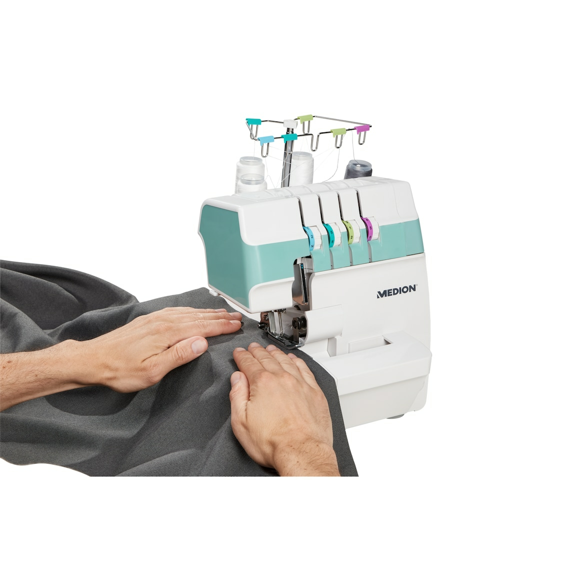 Ręce szyją szarą tkaninę na białej i turkusowej owerlokownicy Medion. Maszyna ma kolorowe prowadnice nici.