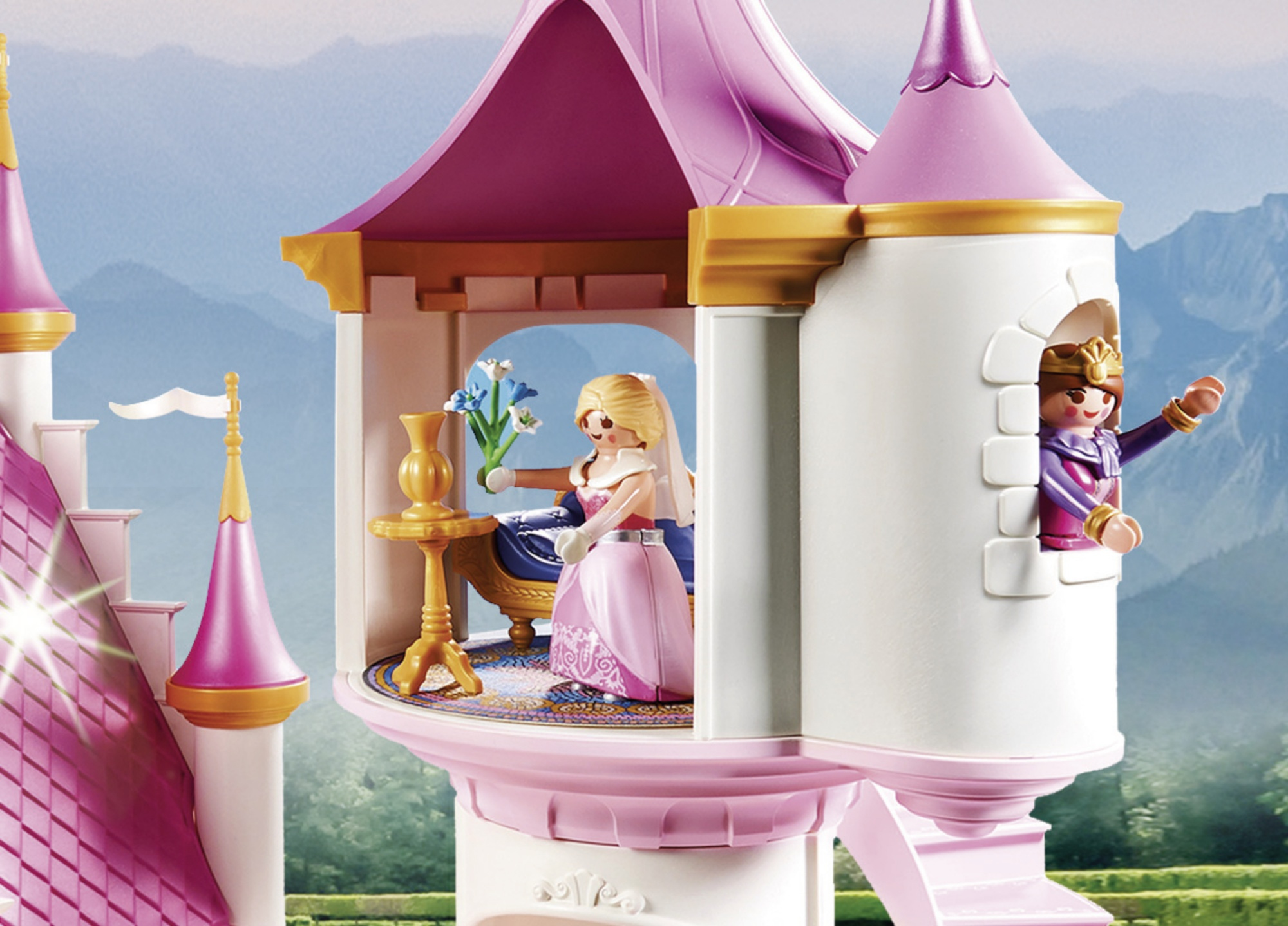 Spielzeugschloss mit Prinzessinnenfiguren. Eine hält Blumen. Eine winkt aus einem Fenster. Rosa-weißes Schloss mit Bergkulisse.