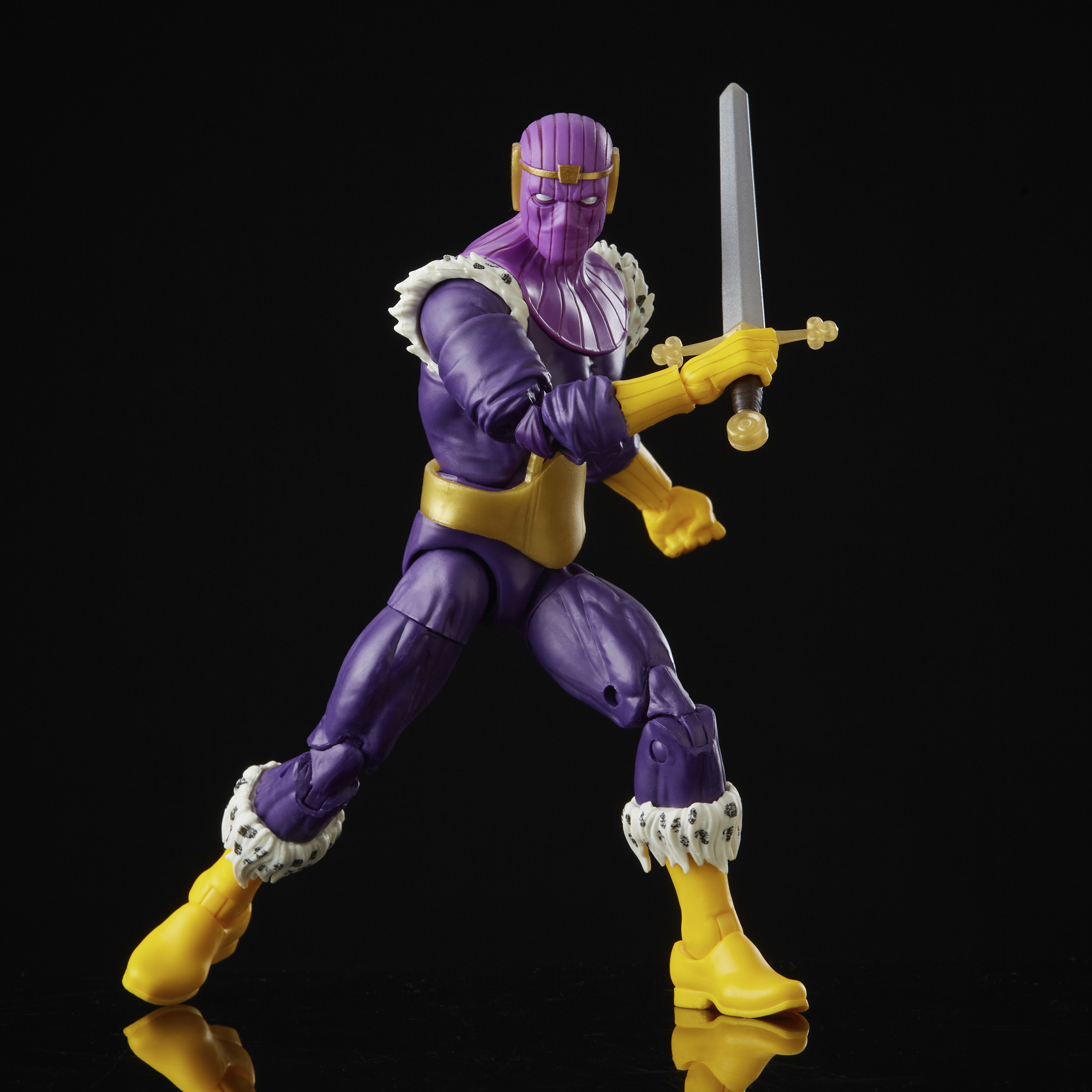 Action figure di un personaggio mascherato viola che tiene una spada, guanti e stivali gialli, bordi in pelliccia bianca, sfondo nero.