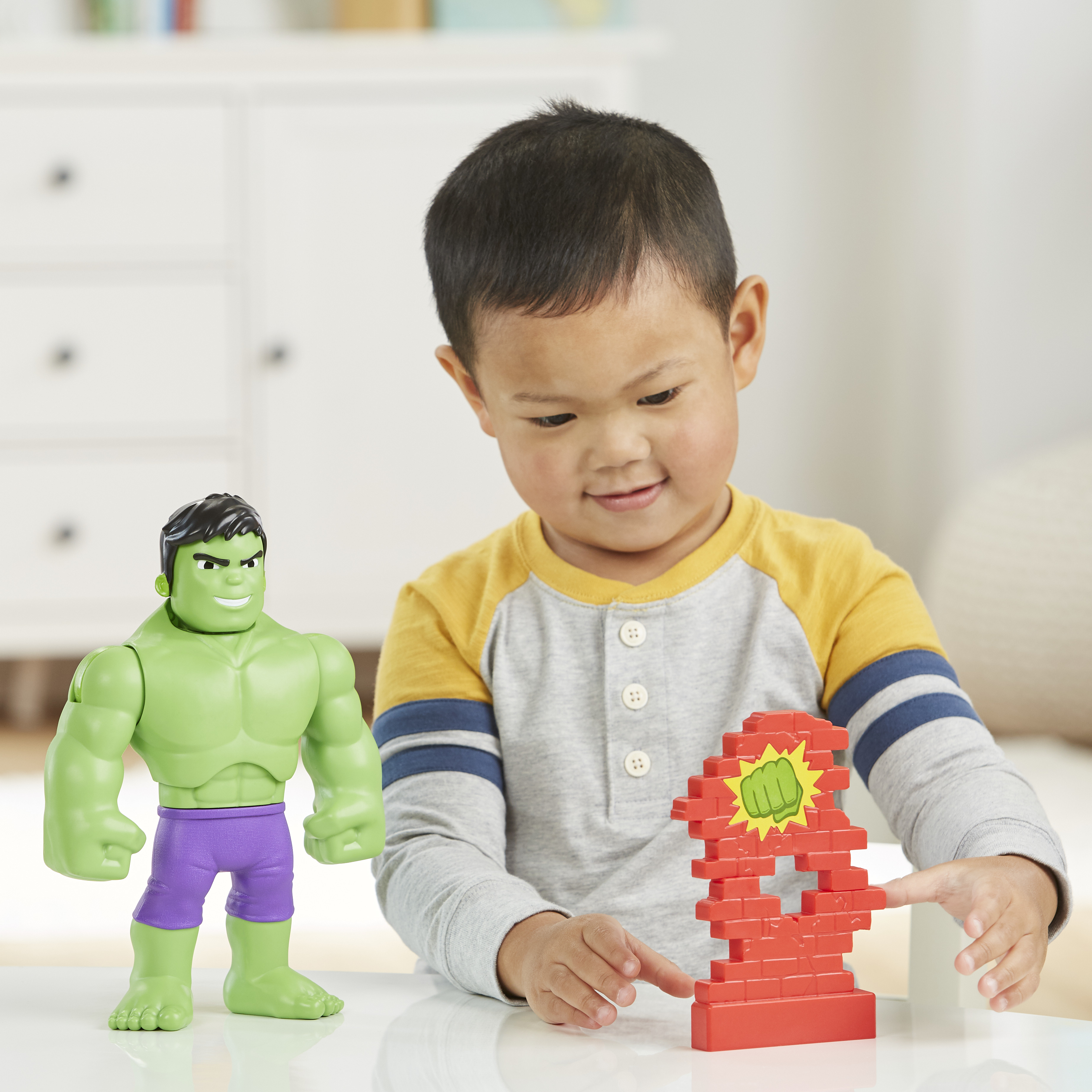 Un bambino gioca con un giocattolo di Hulk e un giocattolo a muro di mattoni. Lo sfondo include una cassettiera bianca.