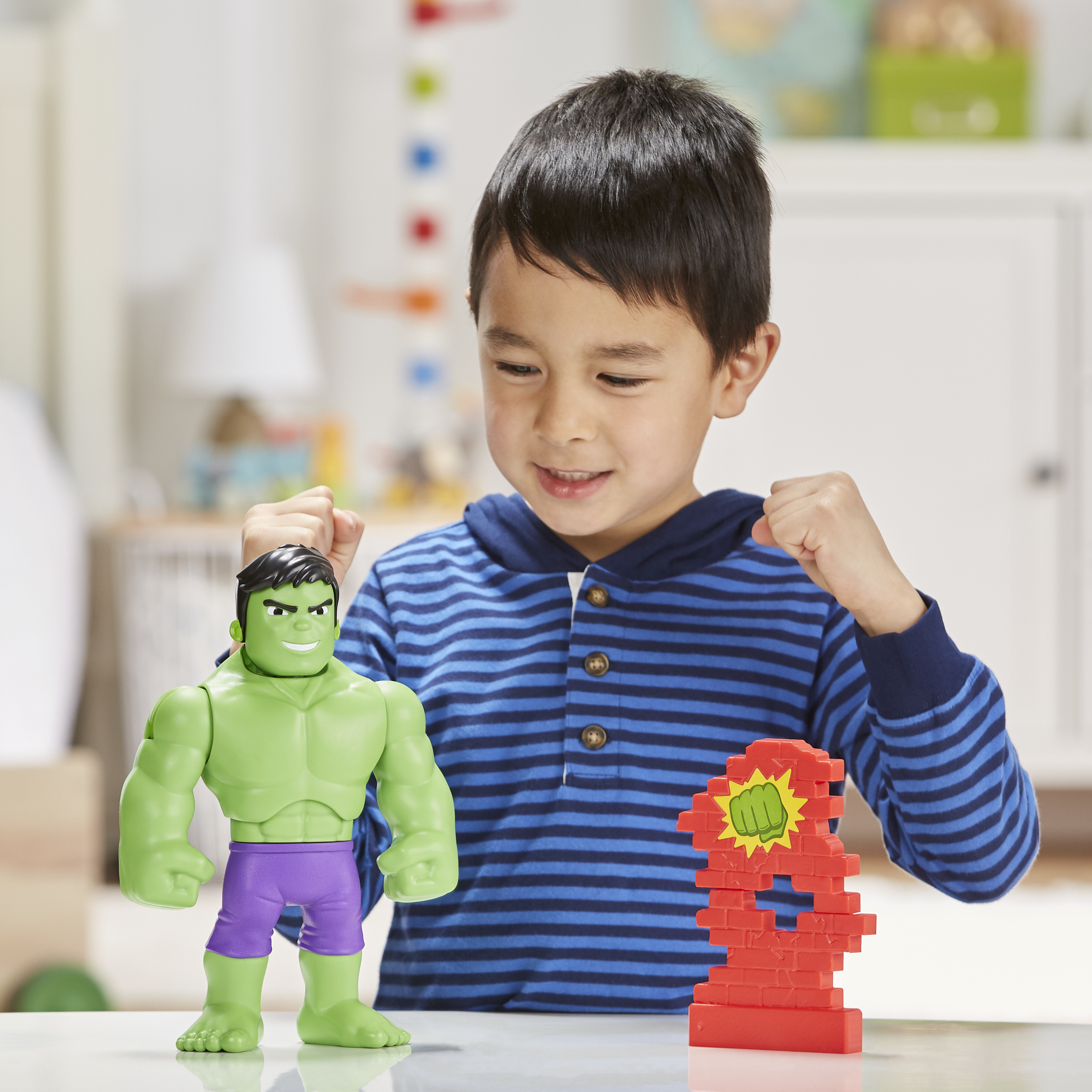 Un ragazzo con un giocattolo di Hulk guarda un giocattolo a muro di mattoni rossi. La figura di Hulk è verde e viola.