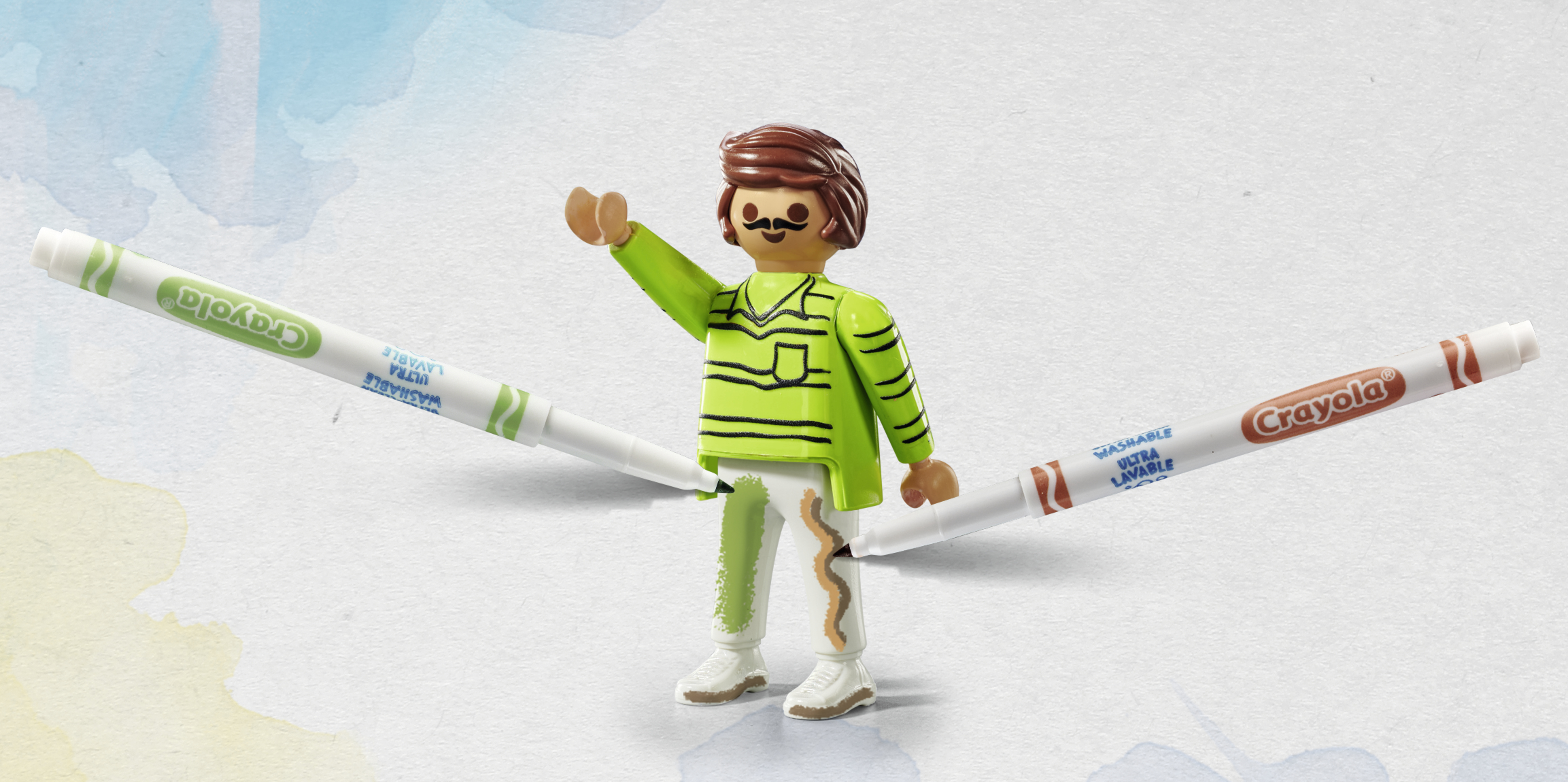Figurka Playmobil z zielonymi i brązowymi markerami. Figurka jest malowana przez markery. Tło to zmycia akwarelowe.