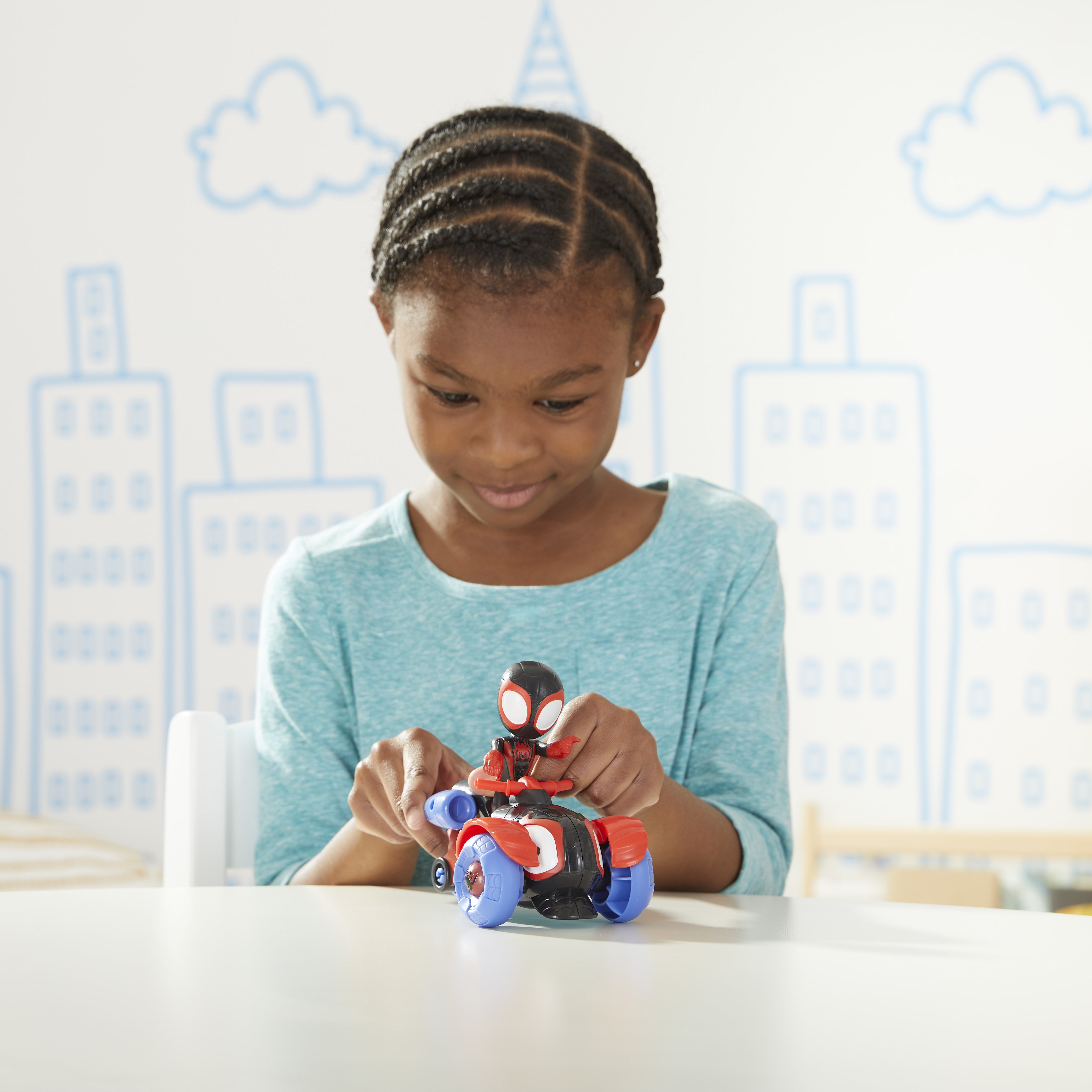 Una bambina gioca con un veicolo giocattolo di Spider-Man. Lo sfondo ha disegni di città e nuvole.