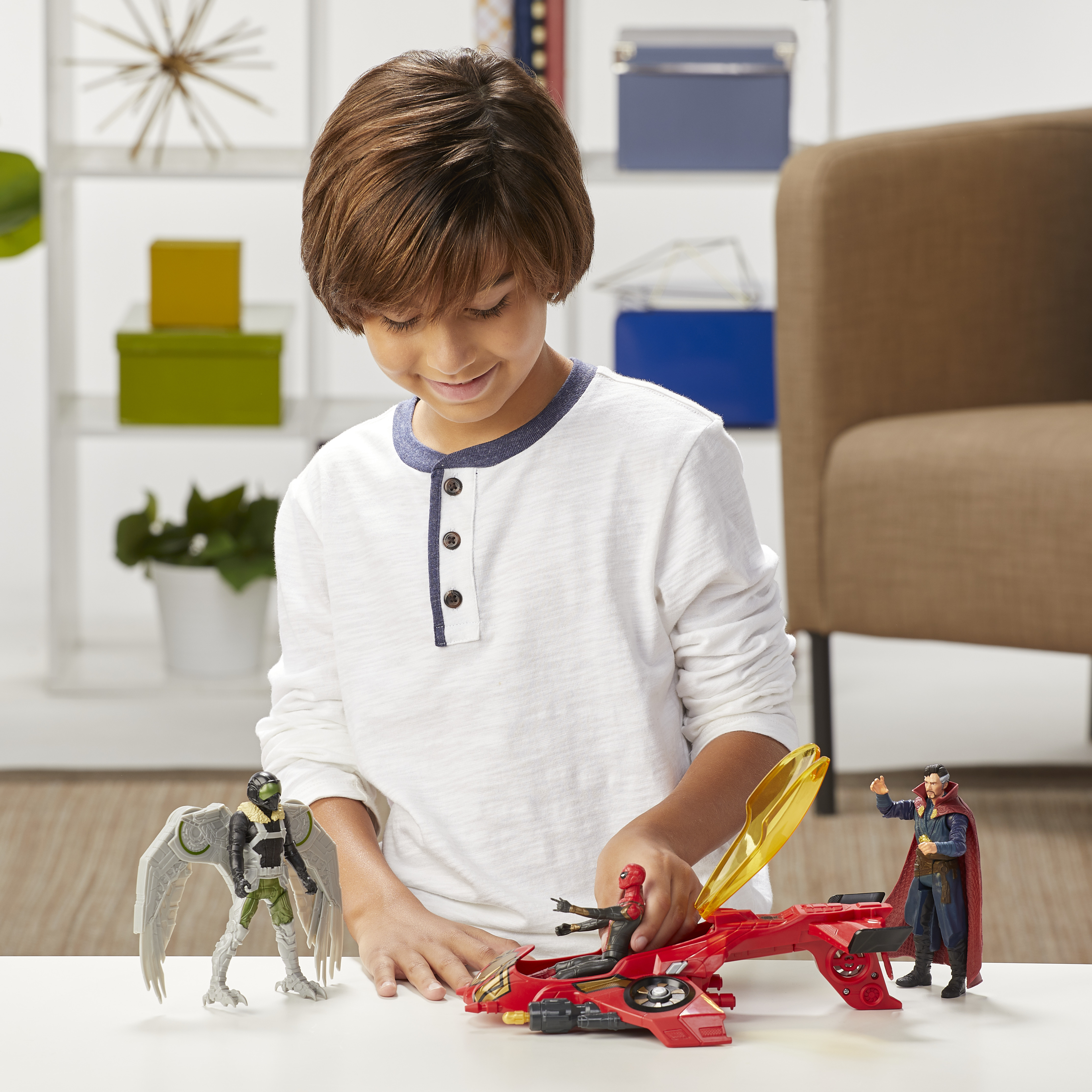 Un ragazzo gioca con action figure di supereroi. Spider-Man su un veicolo rosso, Dr. Strange e Vulture su un tavolo bianco.
