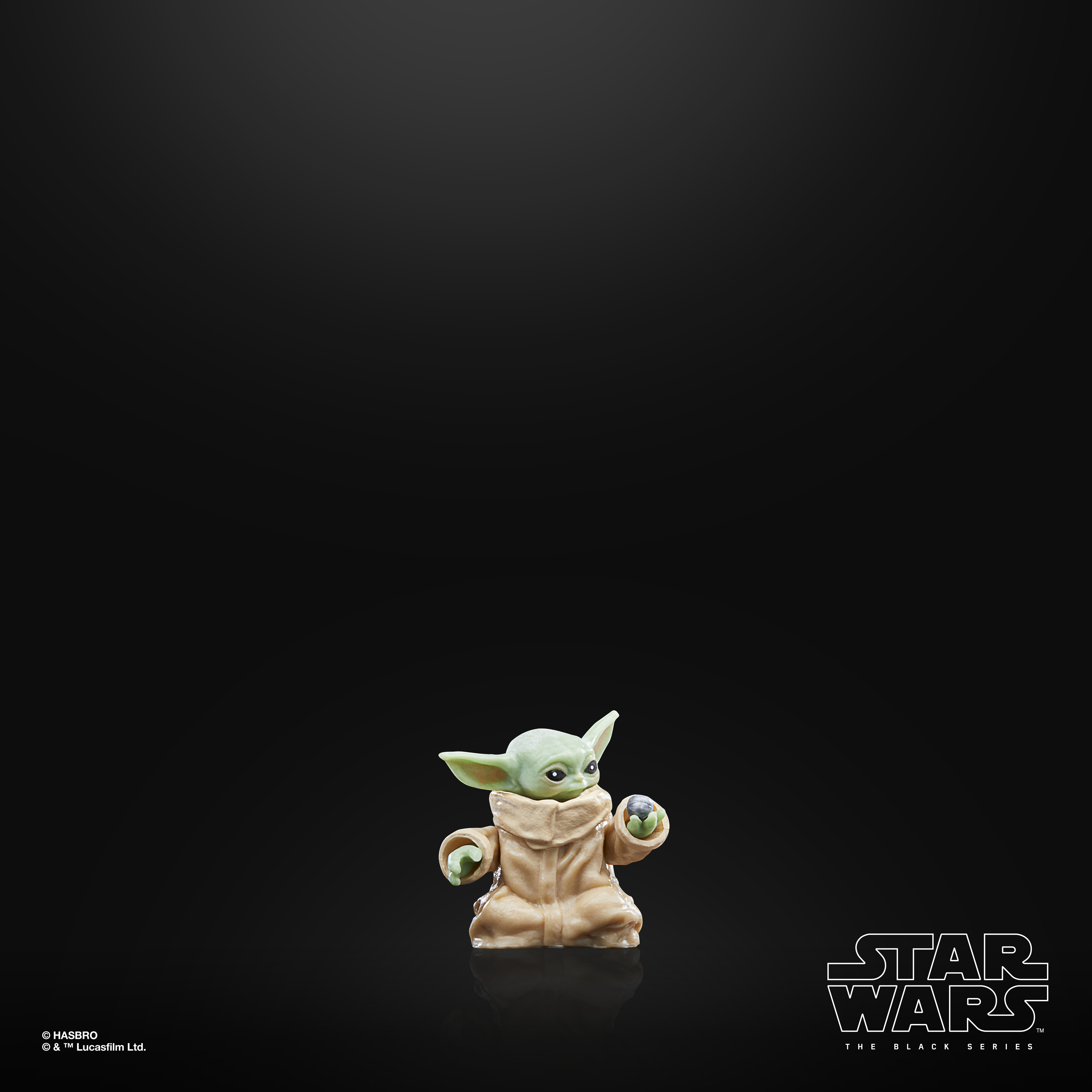 Una statuetta di Baby Yoda, pelle verde, mantello beige, tiene una palla d'argento, su sfondo nero. Logo Star Wars in basso.