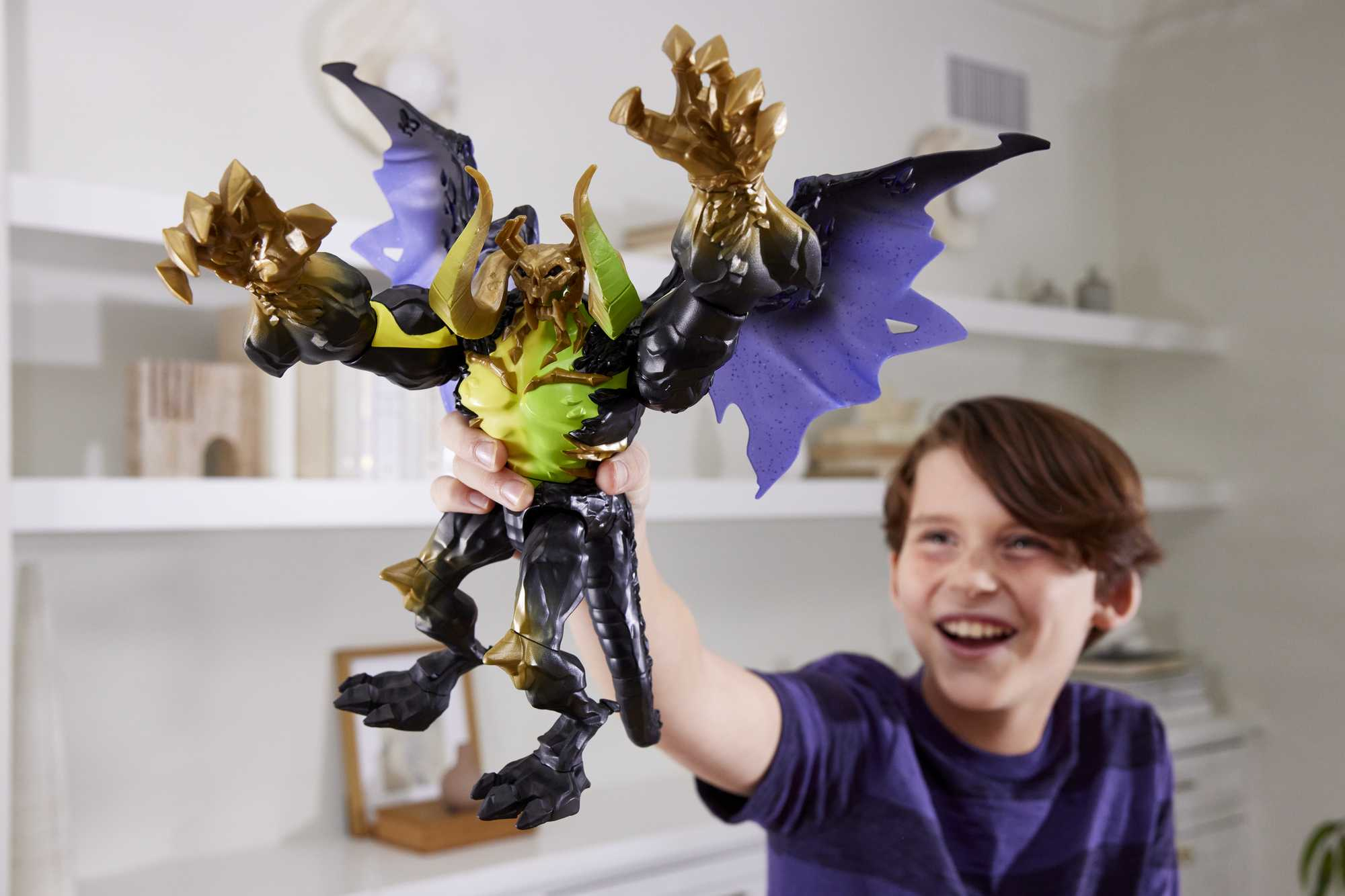 Chłopiec trzyma zabawkę smoka. Zabawka jest czarna, złota i fioletowa, ze skrzydłami, rogami i dużymi pazurami. Chłopiec się uśmiecha.