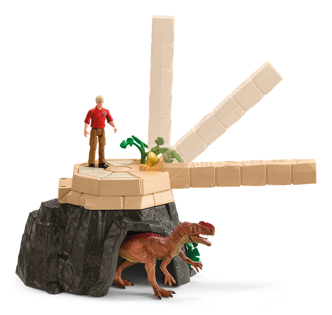 Een speelgoedscène toont een man, een dinosaurus en een structuur. De dinosaurus komt uit een grot. Een man staat bovenaan. De structuur is beige.
