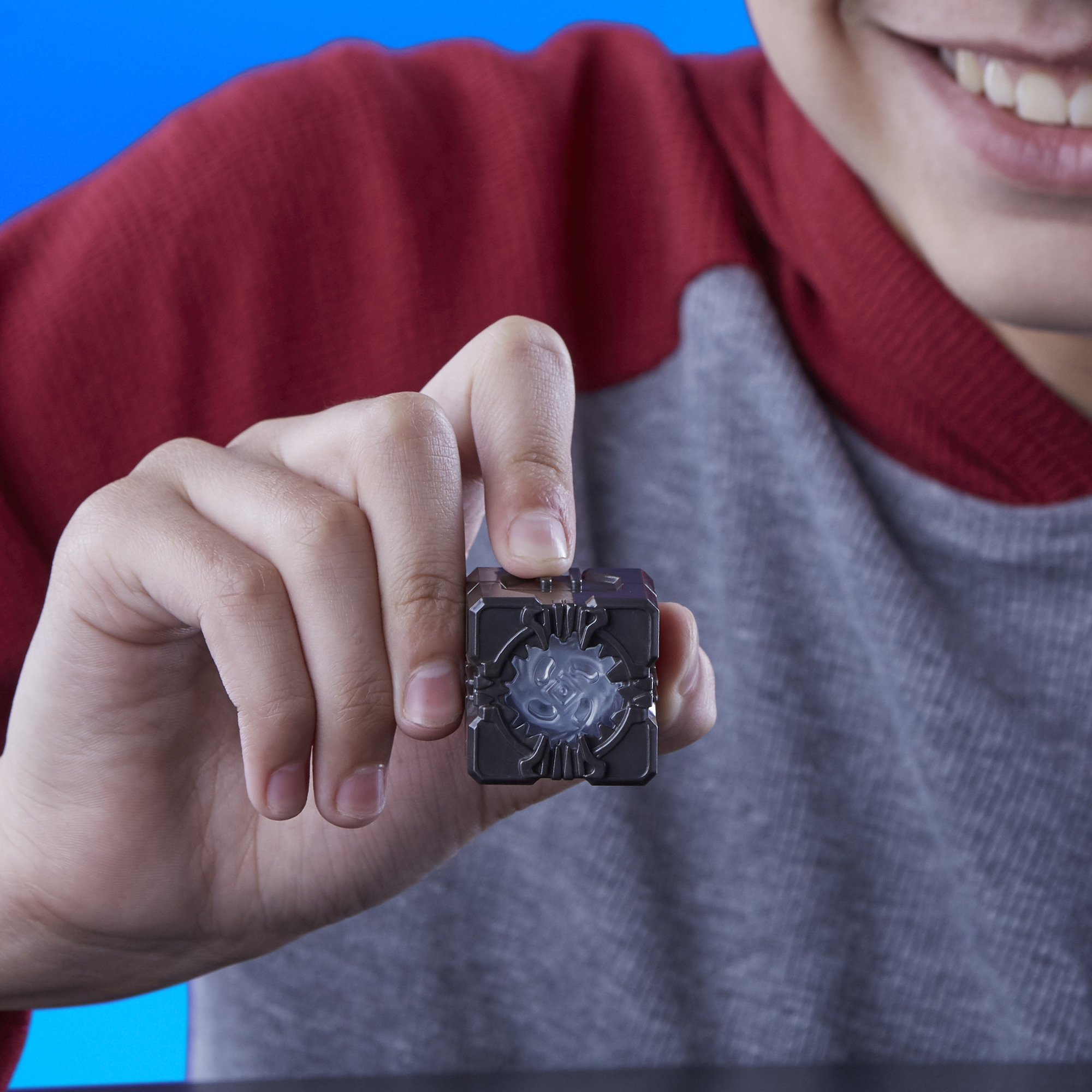 Una persona tiene in mano un cubo nero con un centro luminoso, sorridendo. Indossa una camicia rossa e grigia, su sfondo blu.