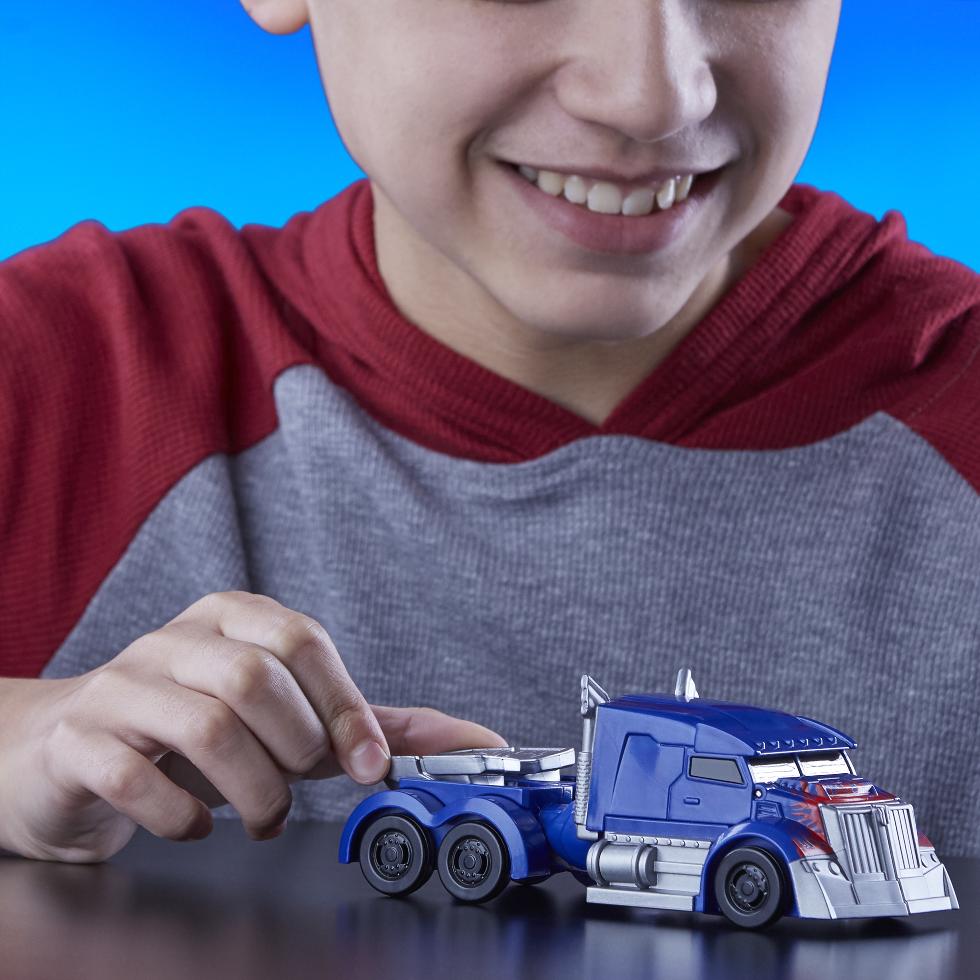 Un ragazzo sorride a un camion giocattolo blu. Tocca il camion su una superficie scura, su sfondo blu.
