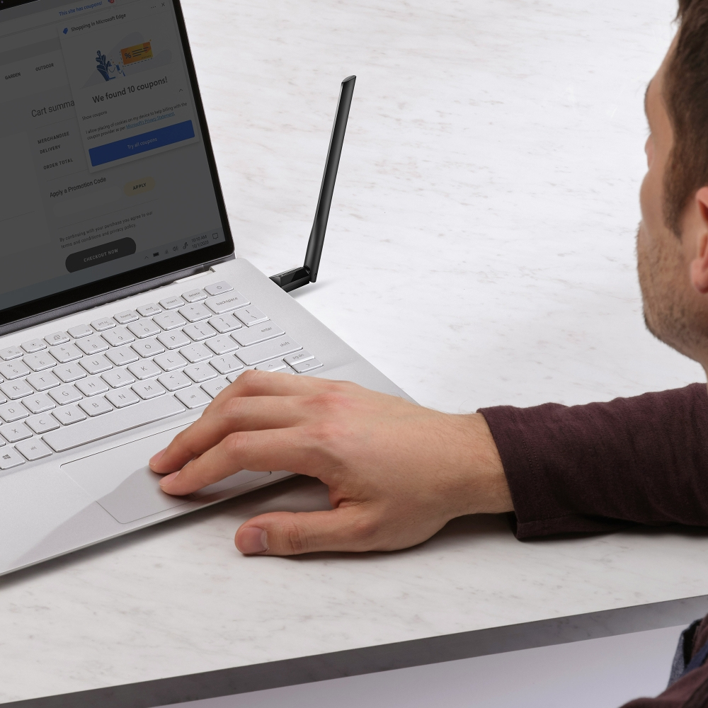 Osoba korzystająca z laptopa. Na ekranie strona zakupowa z kuponami. Podłączona czarna antena. Ręka osoby na touchpadzie.