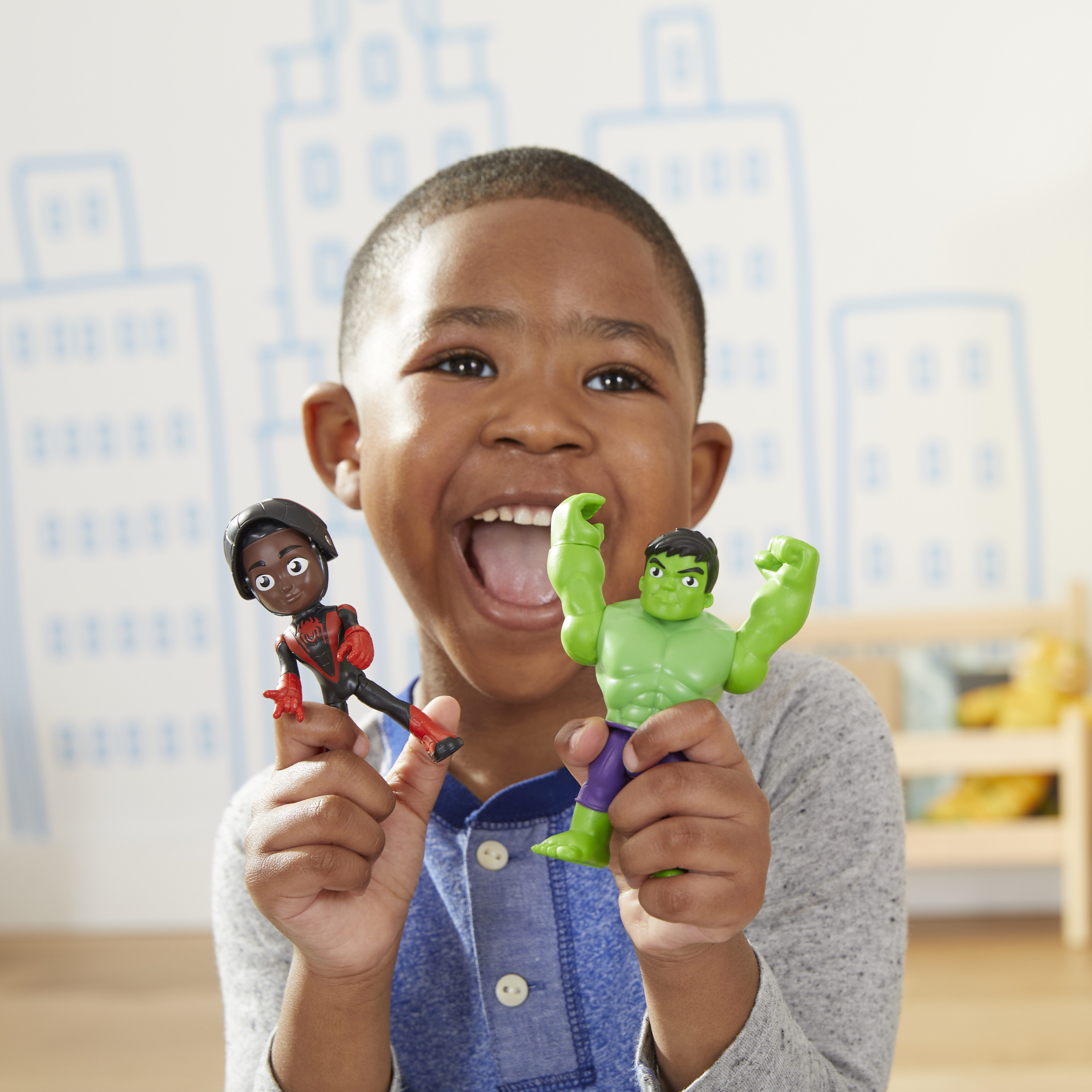 Un ragazzo sorridente tiene in mano un giocattolo di Spider-Man e Hulk. Lo sfondo ha i contorni degli edifici.